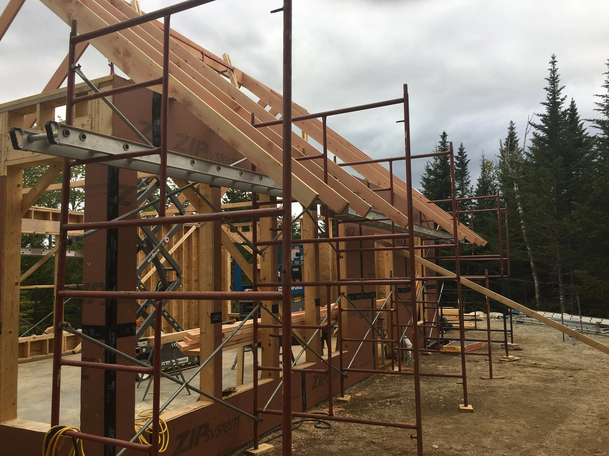 Wood framing of a building under construction with scaffolding and trees in the background.