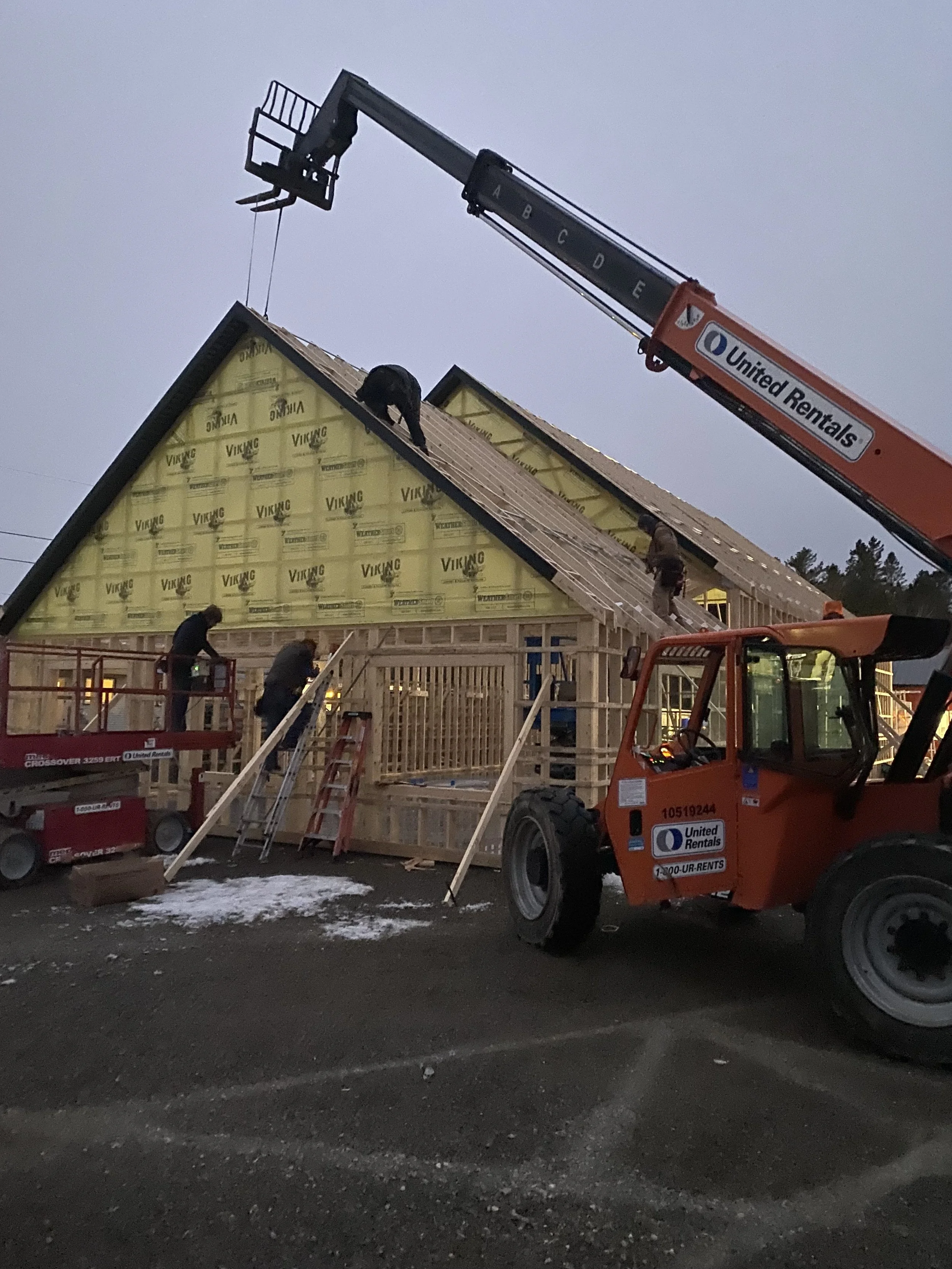 Construction workers building a house, with a crane lifting materials on a partially built roof.