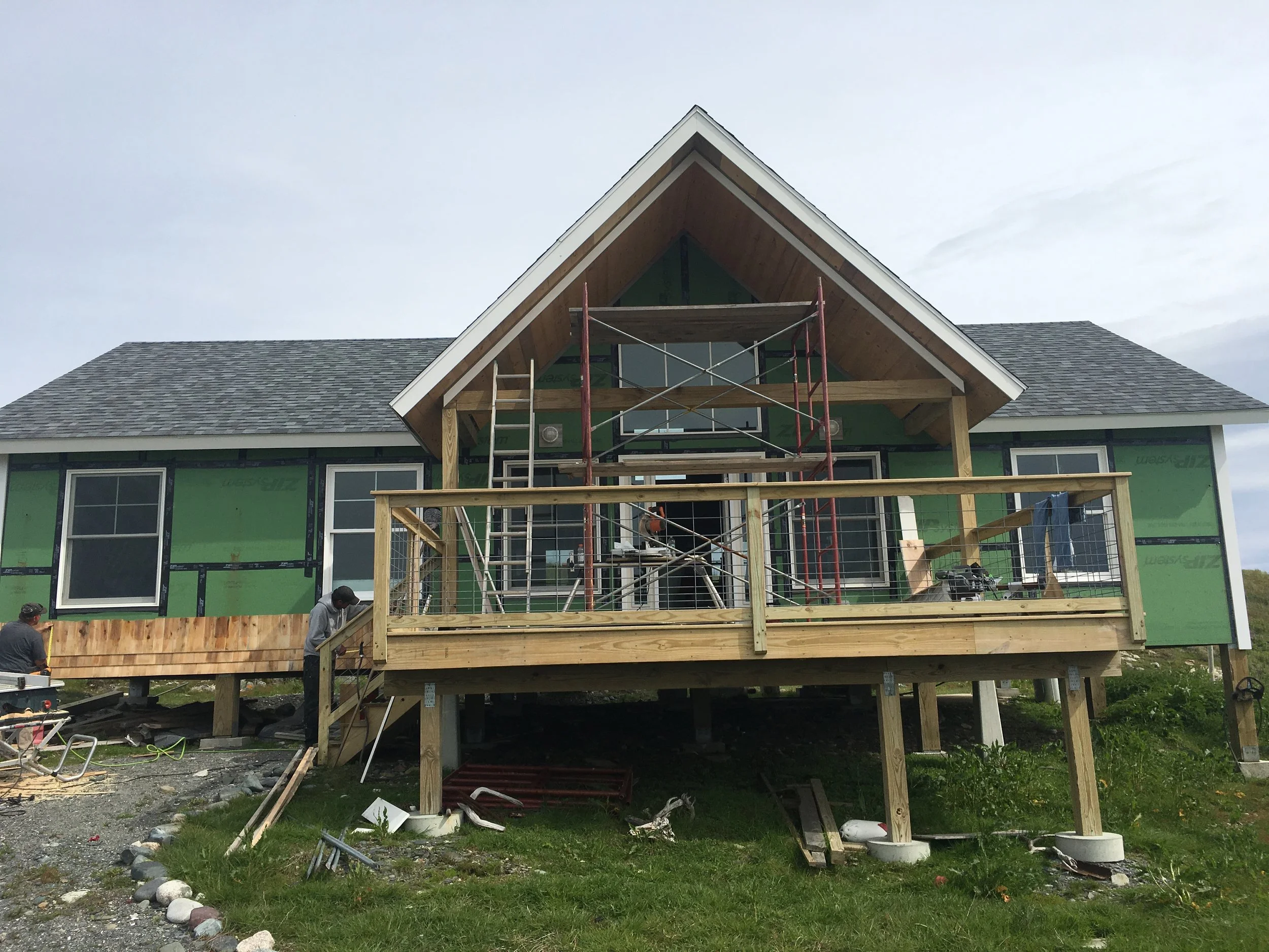 House under construction with scaffolding and workers on the porch.