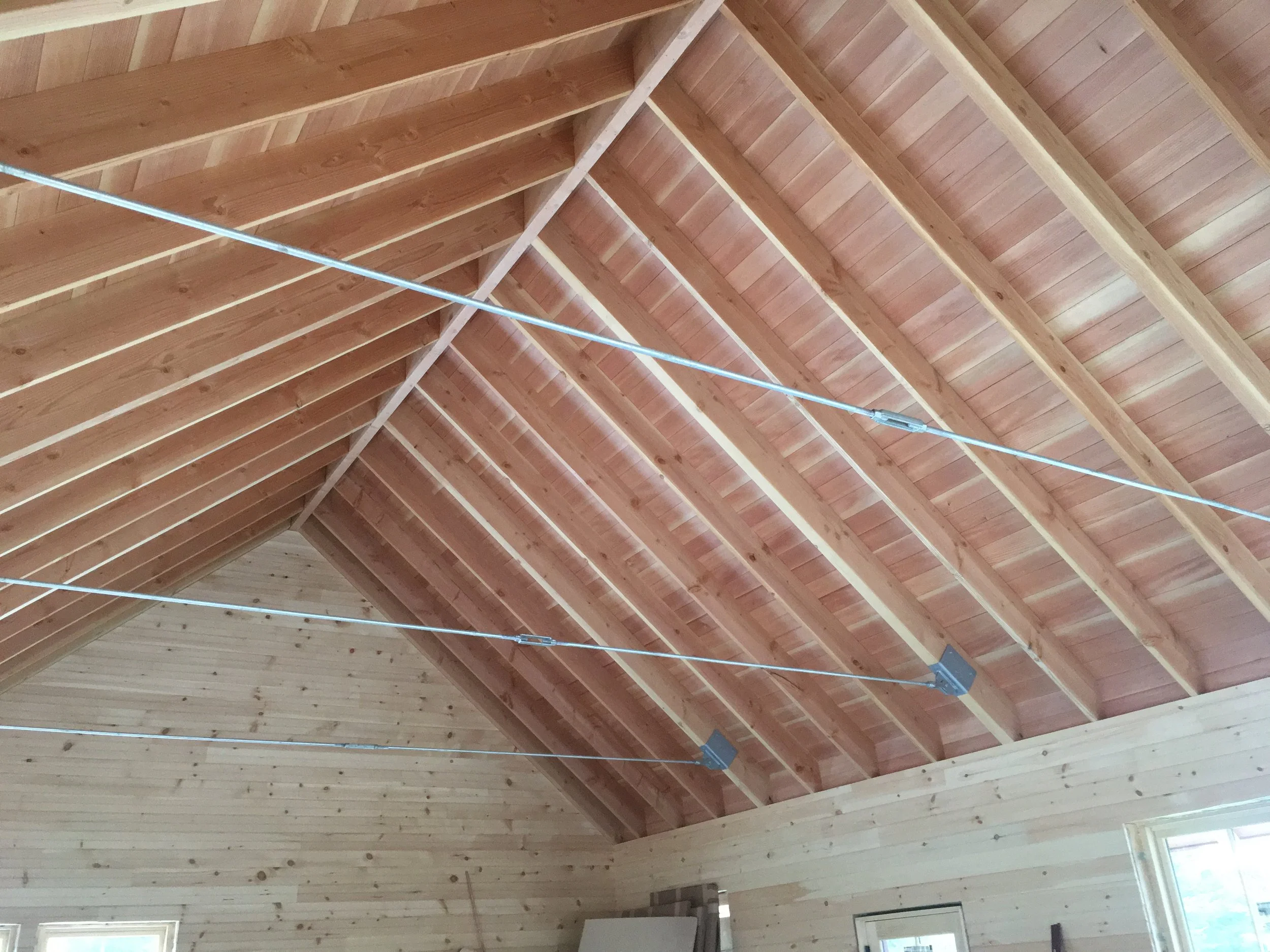 Interior view of a wooden ceiling with exposed beams and metal hanging wires in a house under construction.