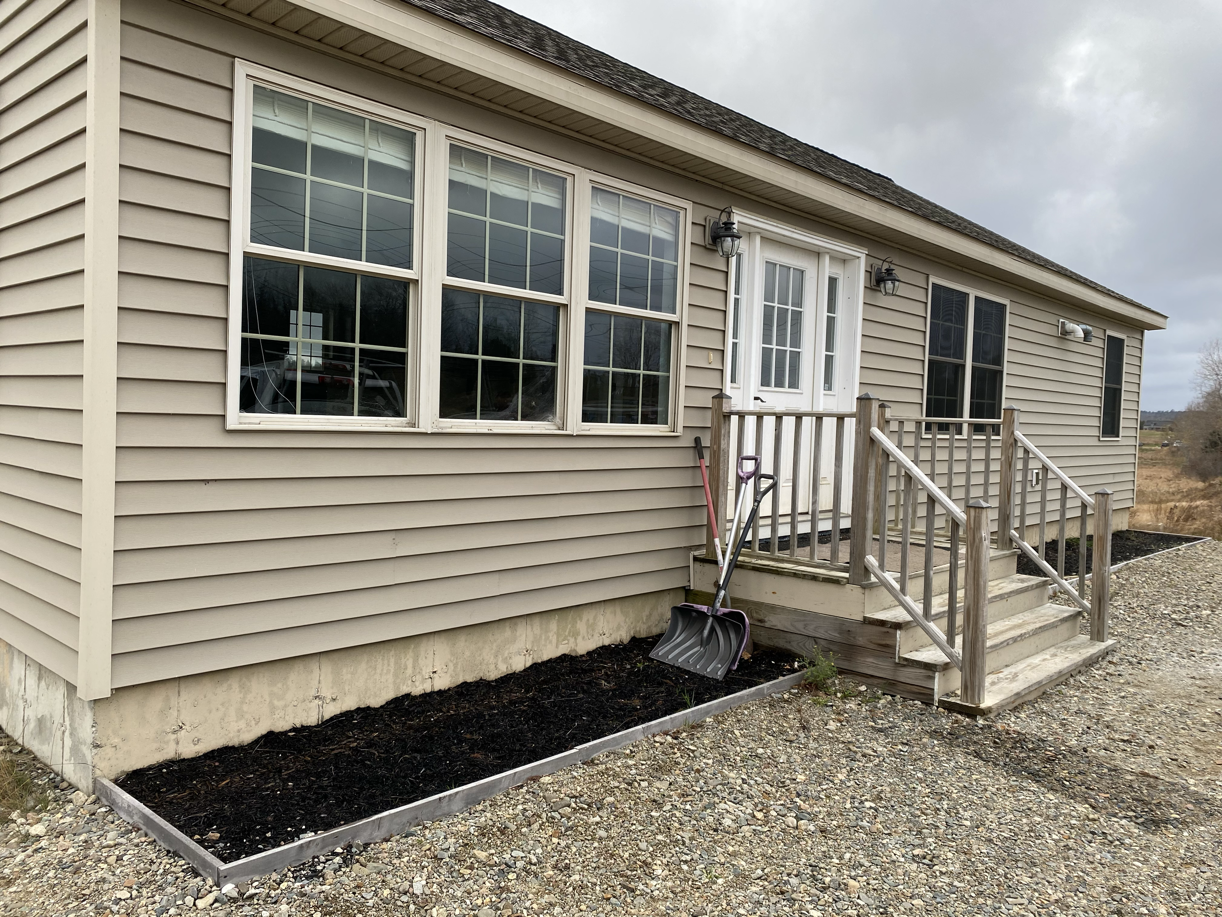 Backyard with a small wooden staircase leading to a white door, beige siding, large windows, and landscaping with black mulch and gravel.
