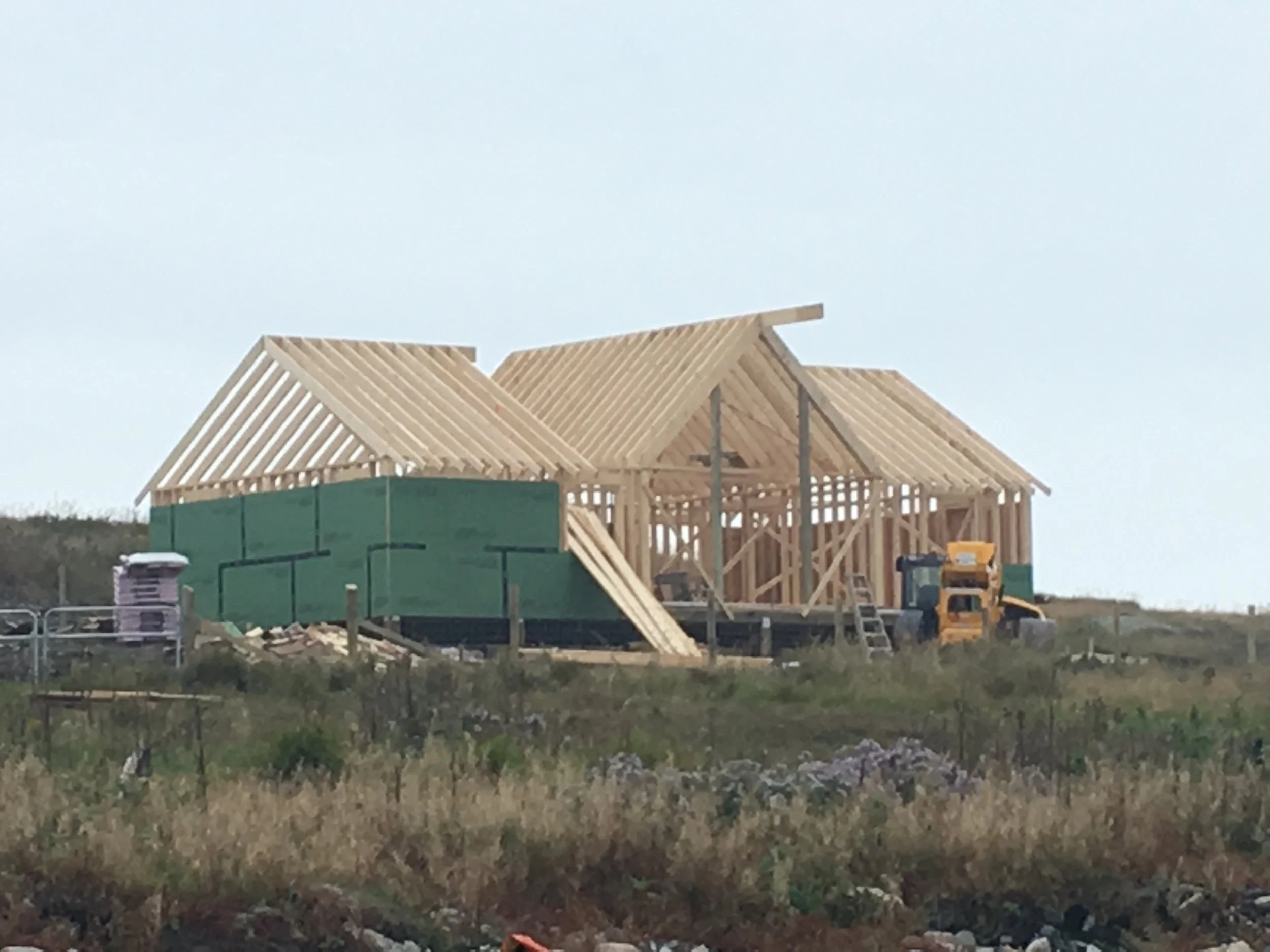 Wooden house under construction on a grassy land with a bulldozer nearby.
