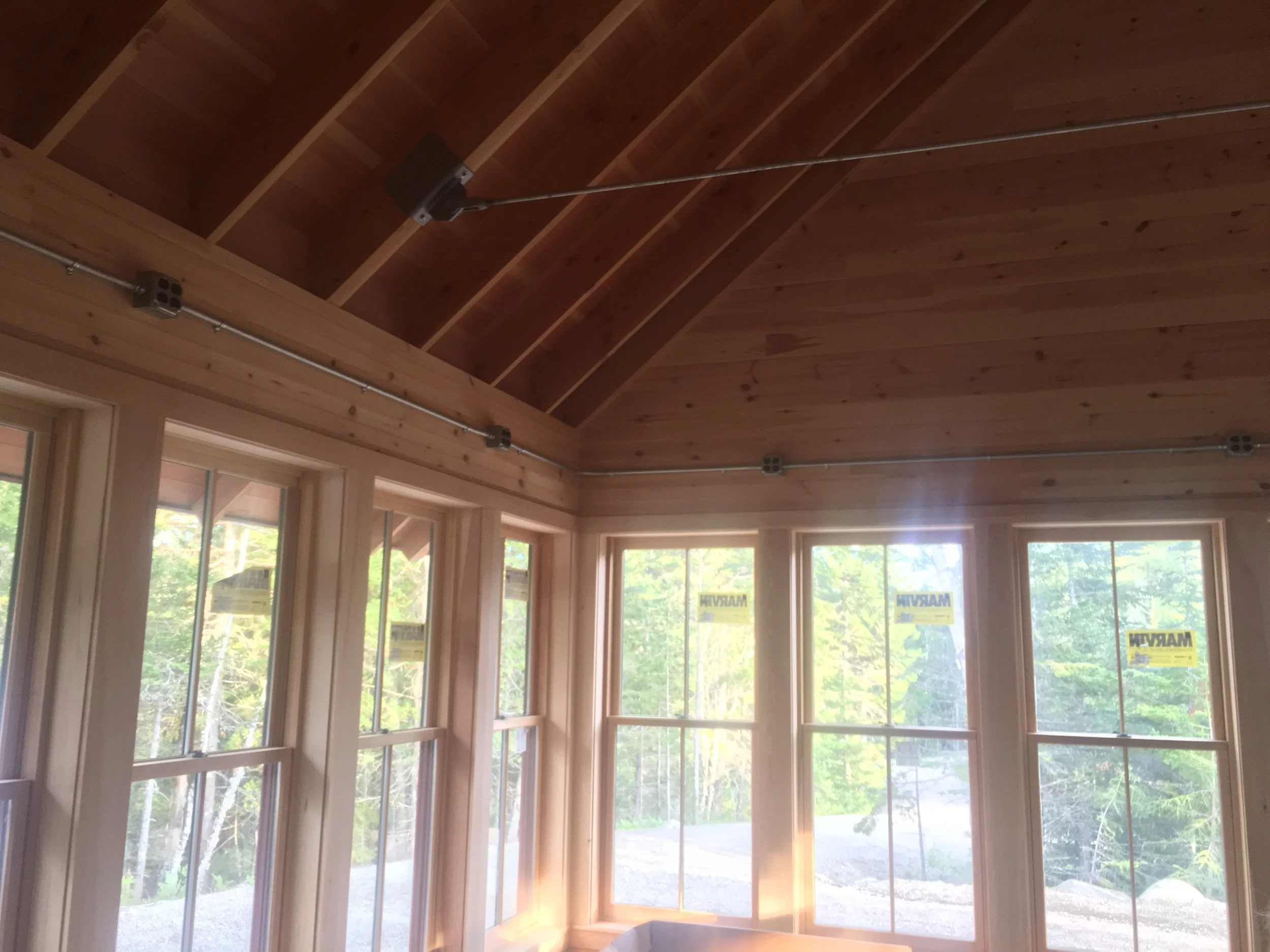 Interior view of a room with large windows, wooden walls, and a vaulted ceiling with wood paneling, during daylight.