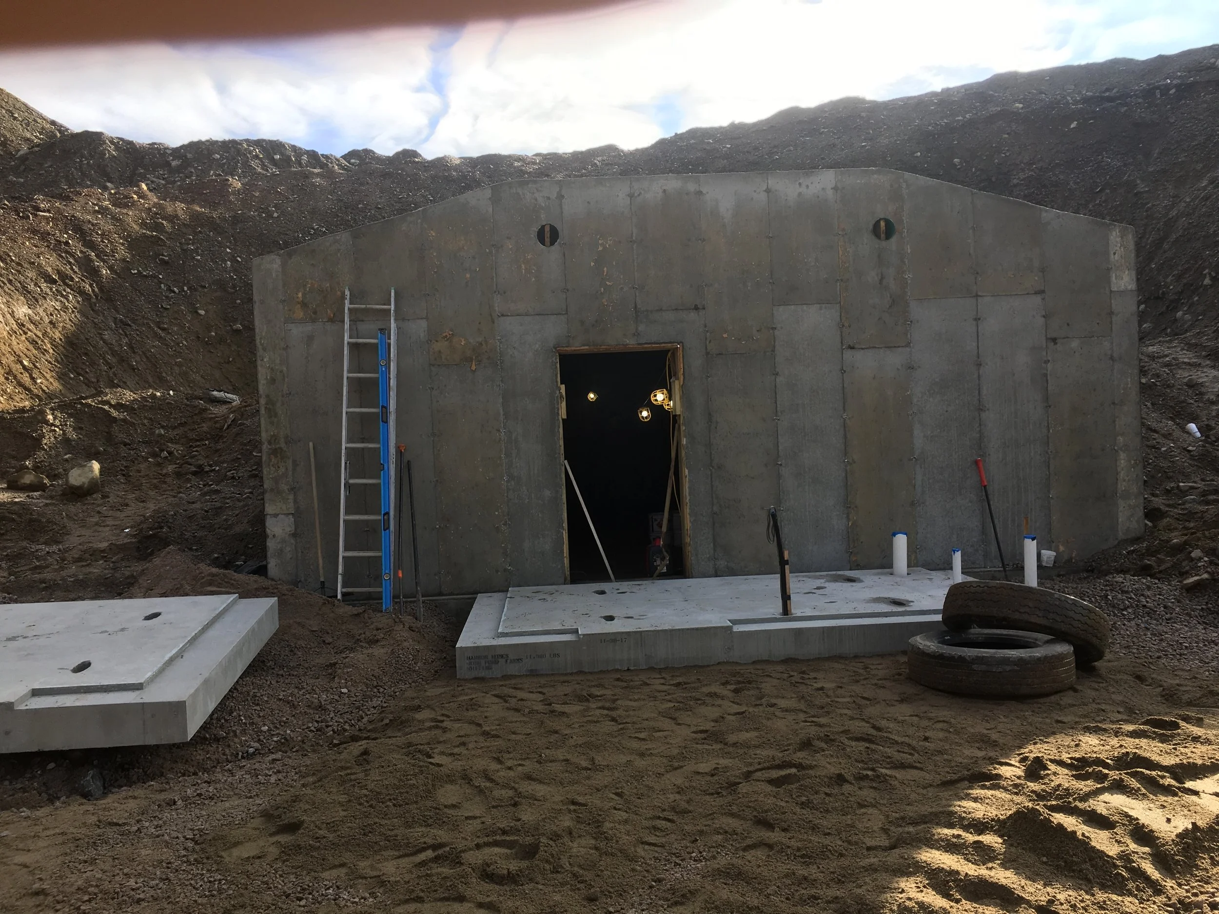 Construction site with a concrete building, ladder, tires, and building materials in a dirt area