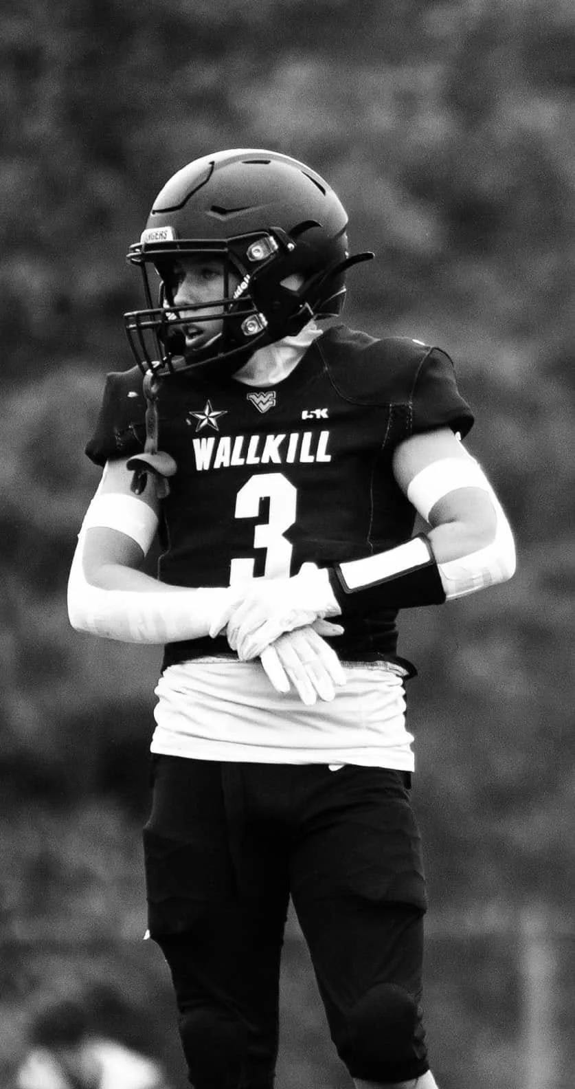 A young football player in uniform with a helmet and gloves, standing on the field.