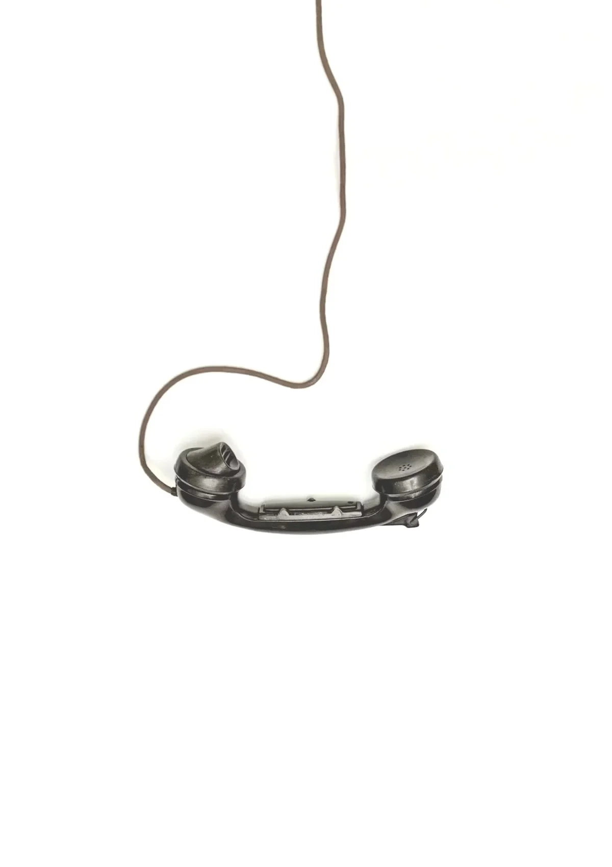 Old black rotary telephone with a cord, positioned to form a minimal outline of a human face in profile.