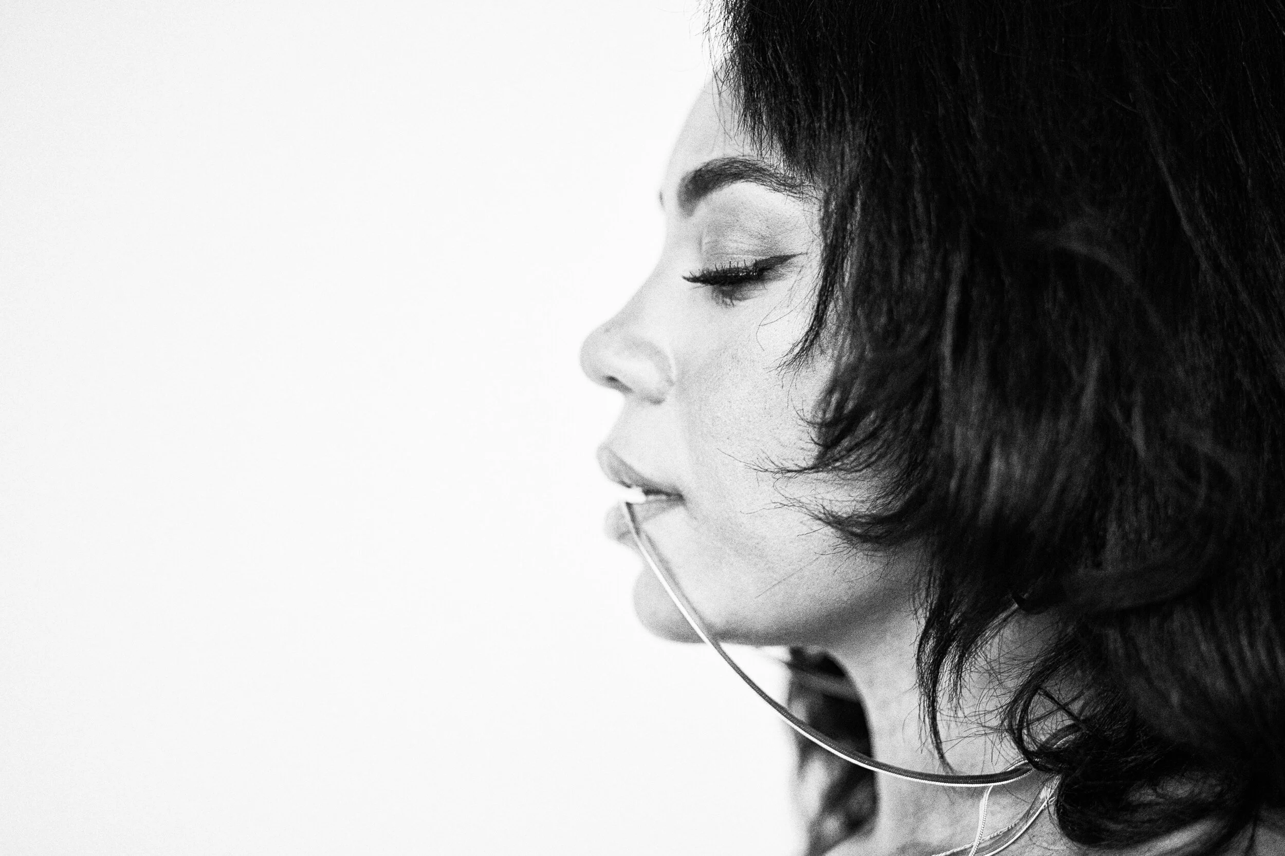 Close-up side profile of a woman with short curly hair, closed eyes, wearing earphones, in black and white.