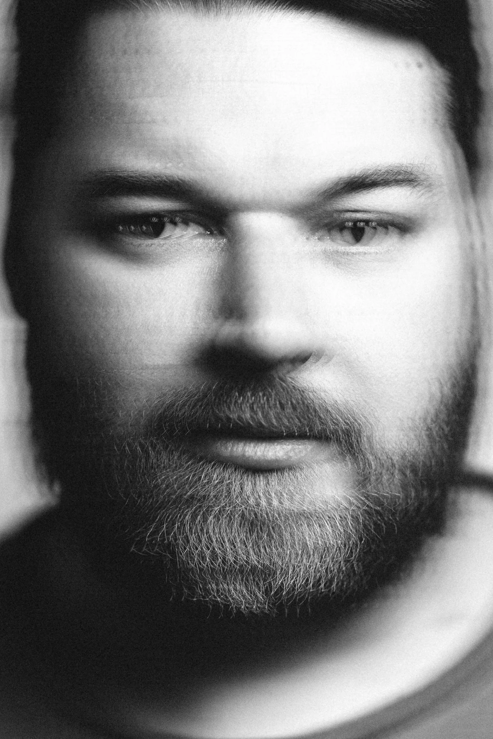 Close-up black and white photograph of a man's face, focusing on his eyes, nose, and beard.