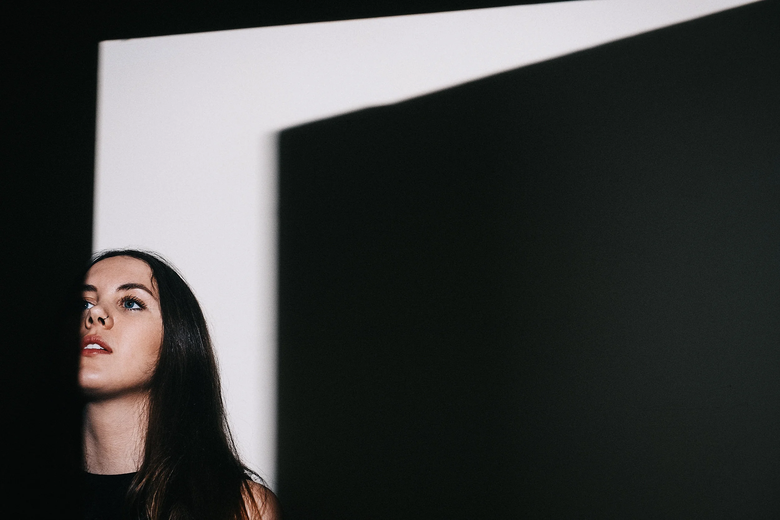 A woman with long dark hair and blue eyes looking upward, partially obscured by a shadow.