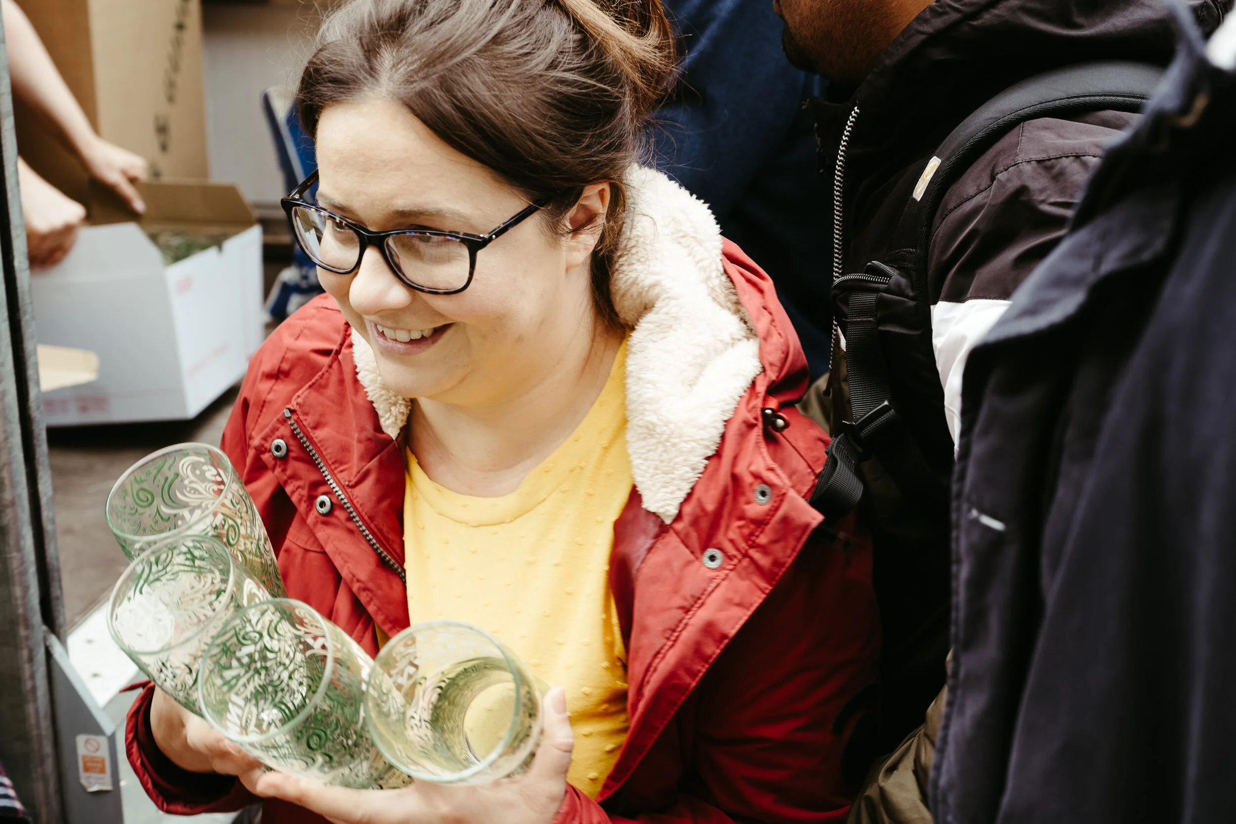 Woman with glasses examining decorative glassware at a store, surrounded by other shoppers.