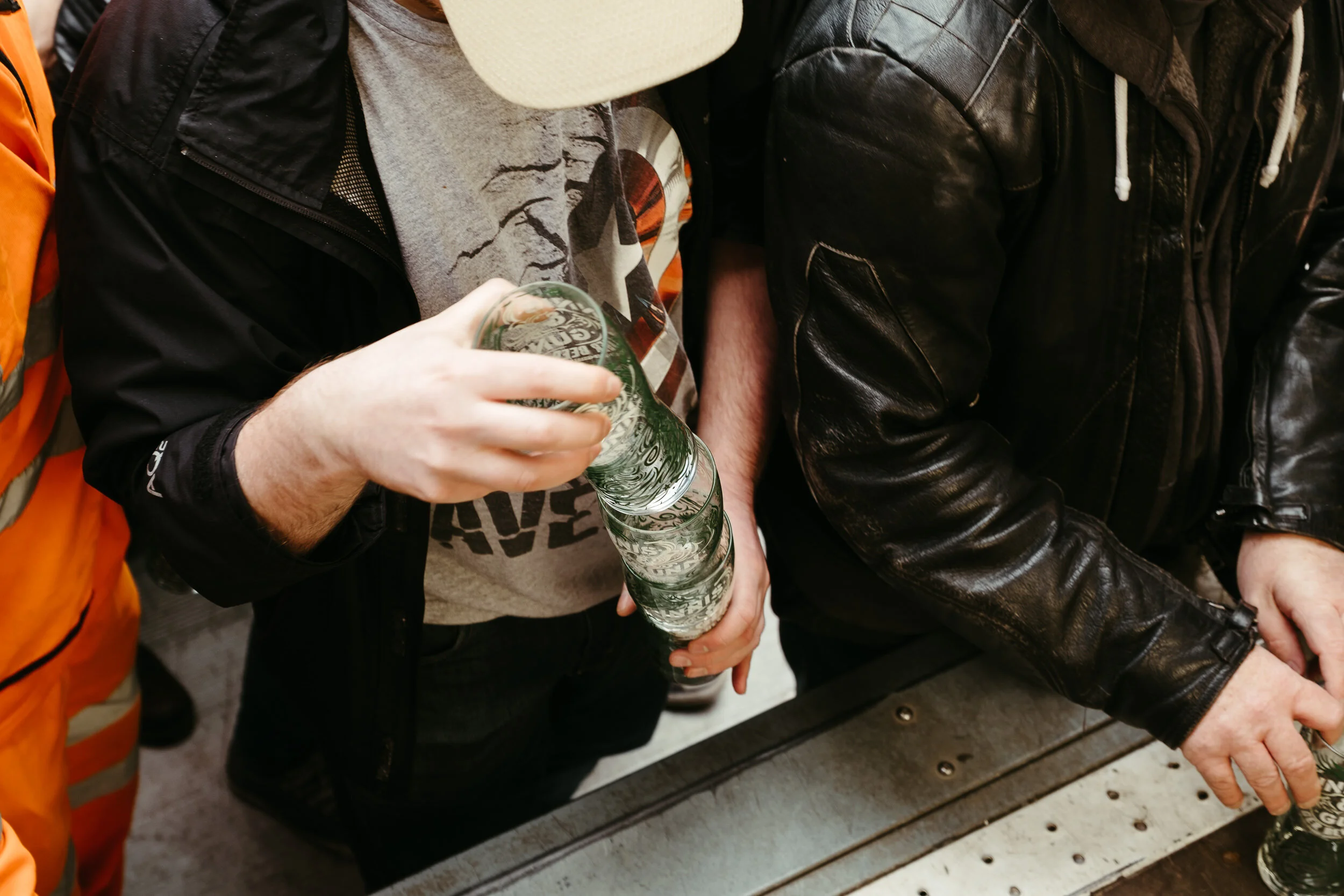 Close-up of a person holding a glass of beer with a crowd around at a bar or festival.