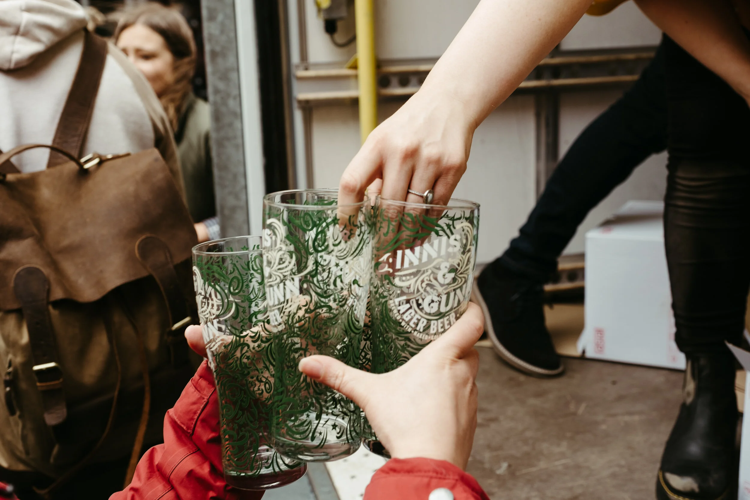 Close-up of a hand reaching into a glass with a green and white decorative pattern, in a restaurant or bar setting. People and kitchen equipment are in the background.