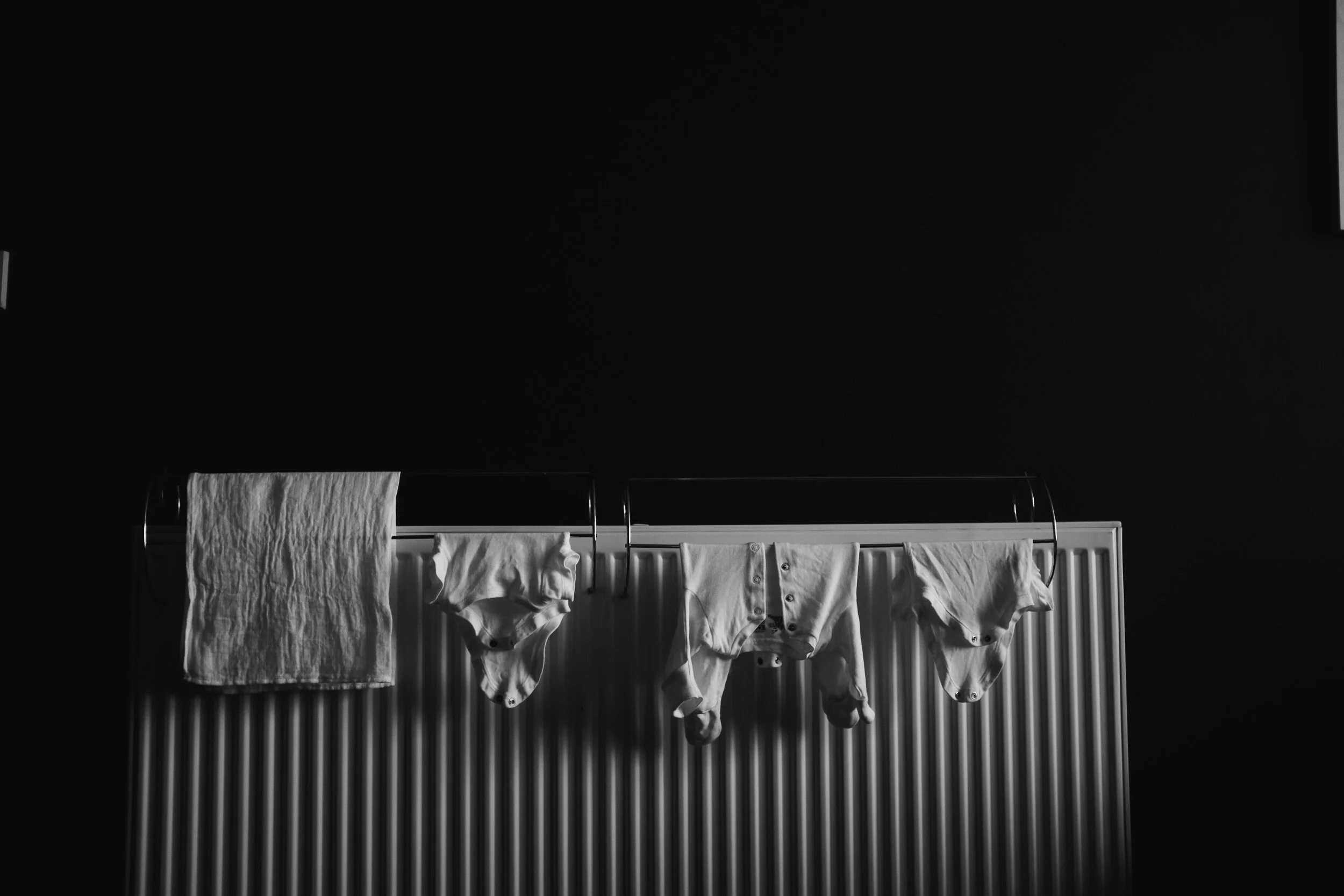Clothes hanging on a drying rack in front of a black wall, with some of the garments obscured by darkness.