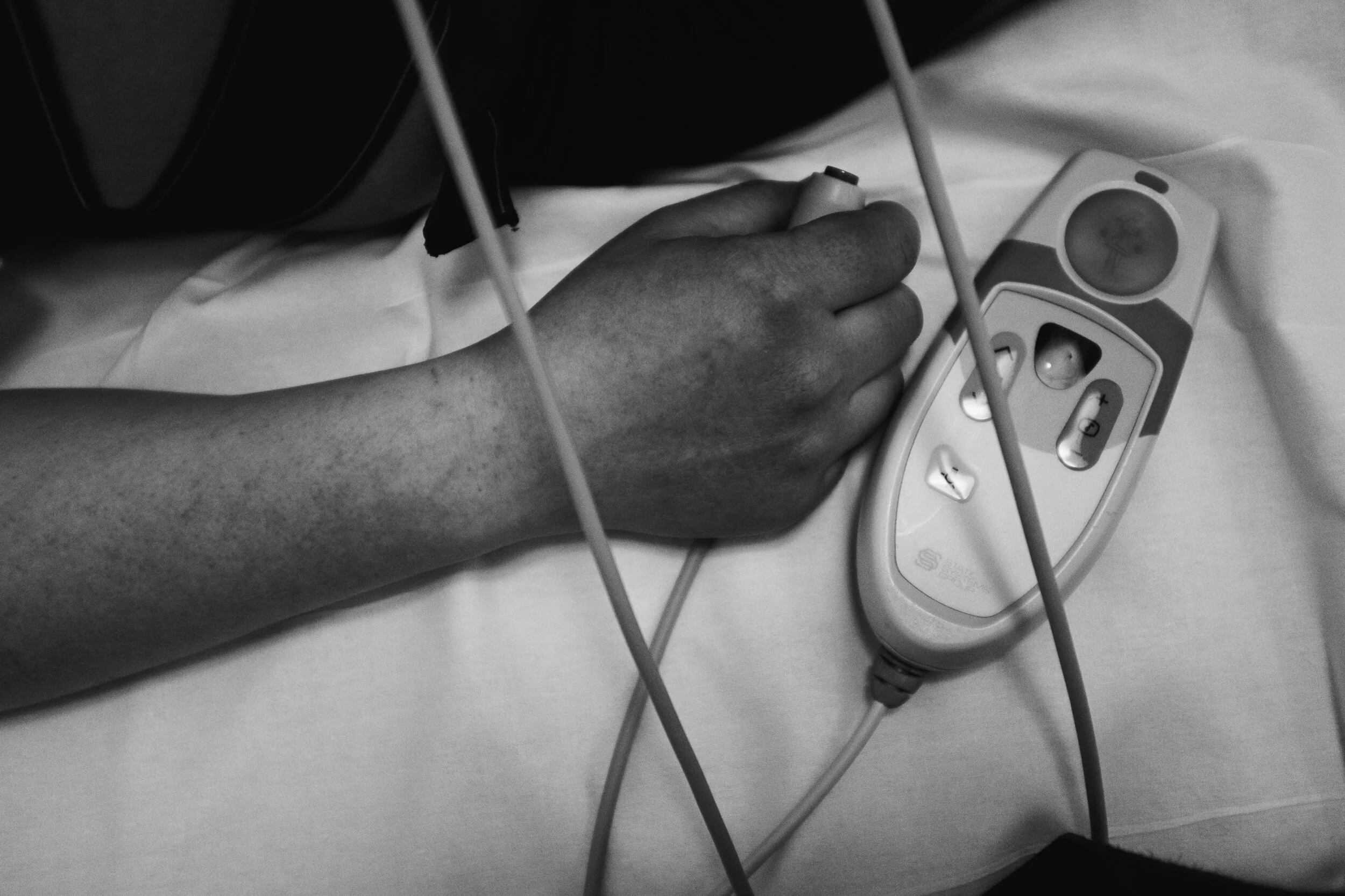 A person lying in a hospital bed with their arm extended, connected to medical monitoring devices.