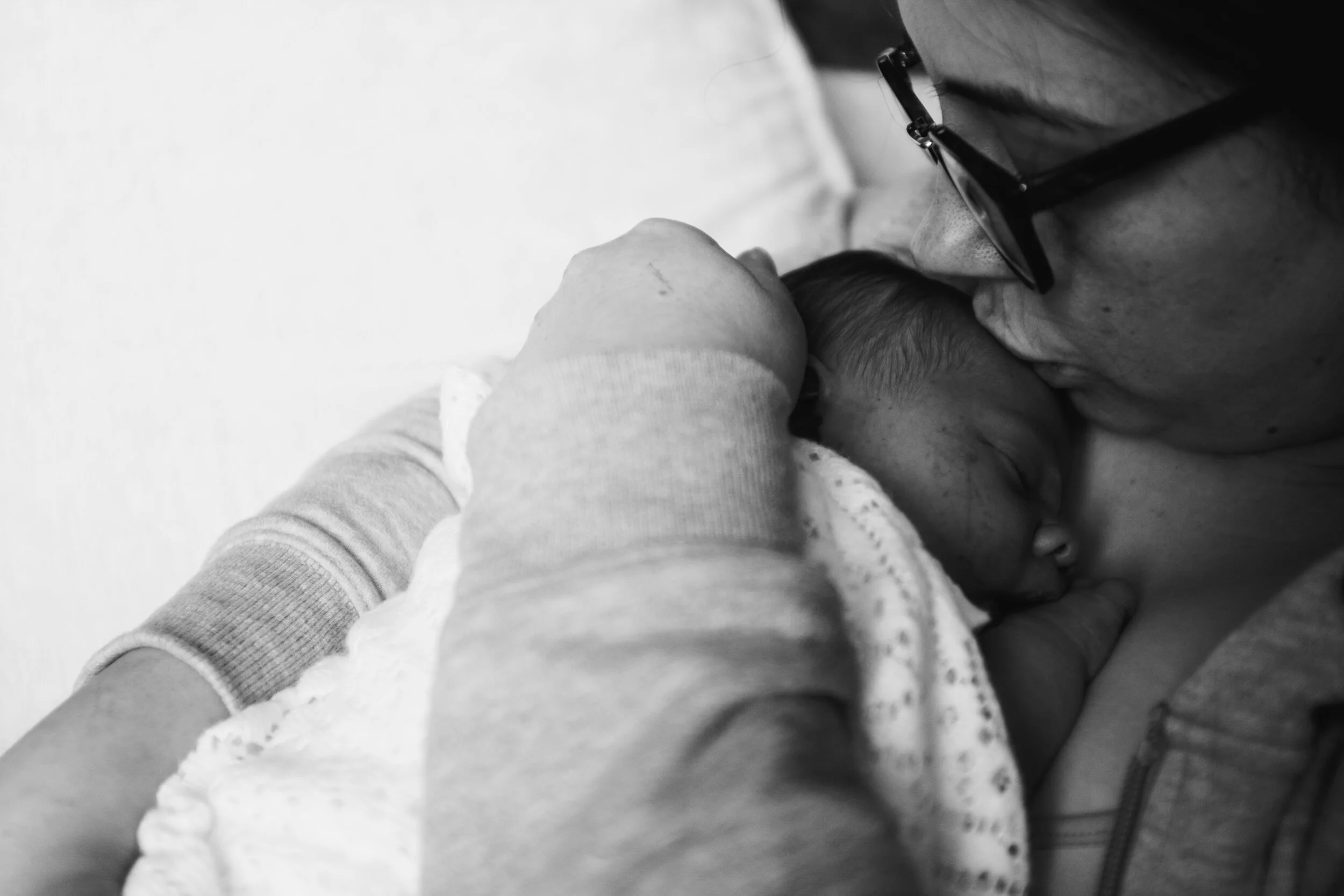 A person wearing glasses gently holds a sleeping baby in their arms.