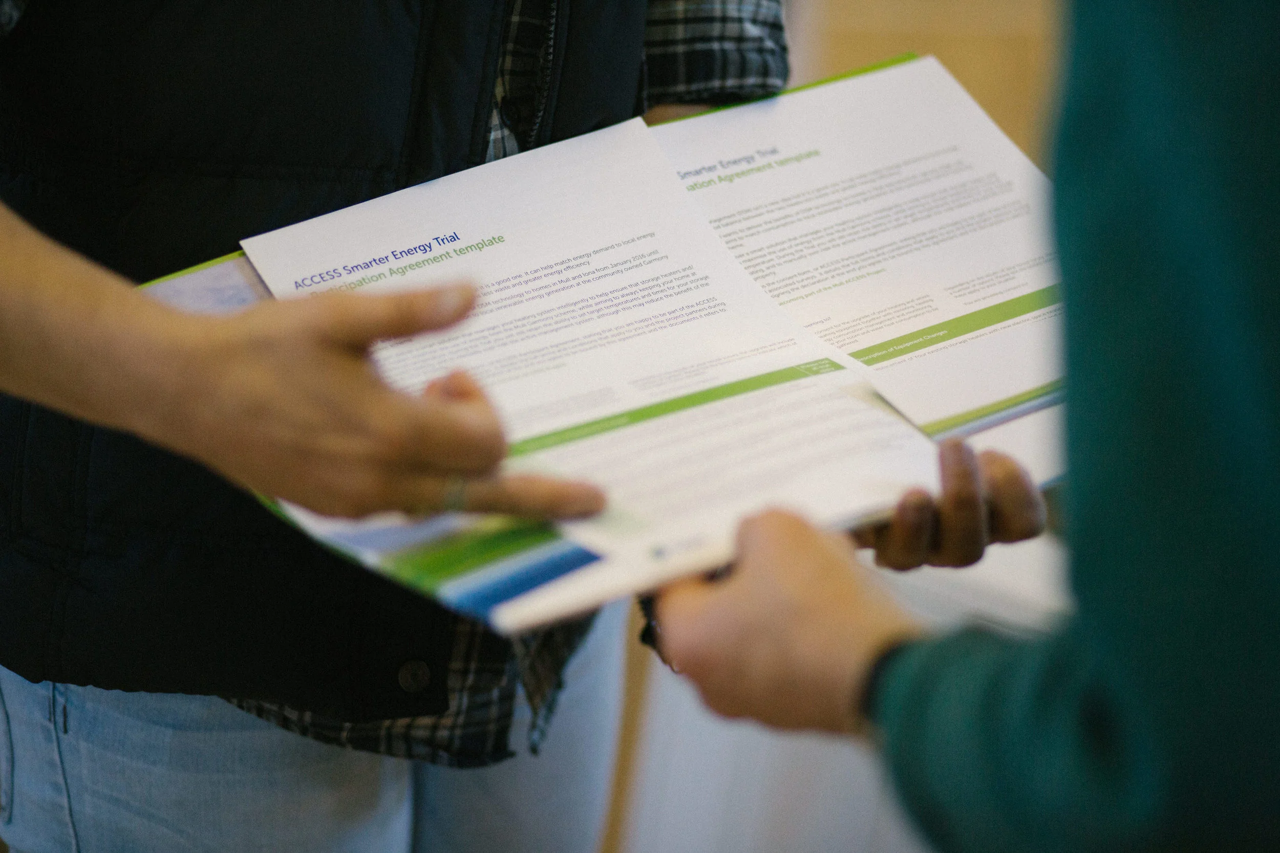 Close-up of a person holding and examining a document titled 'ACCESS Smarter Energy Trial Participation Agreement template,' with other papers partially visible.