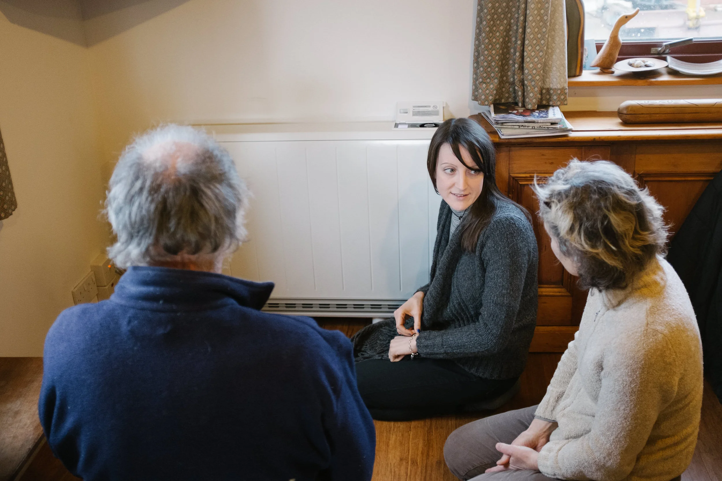 Four people sitting on the floor in a circle, engaging in conversation in a cozy room.