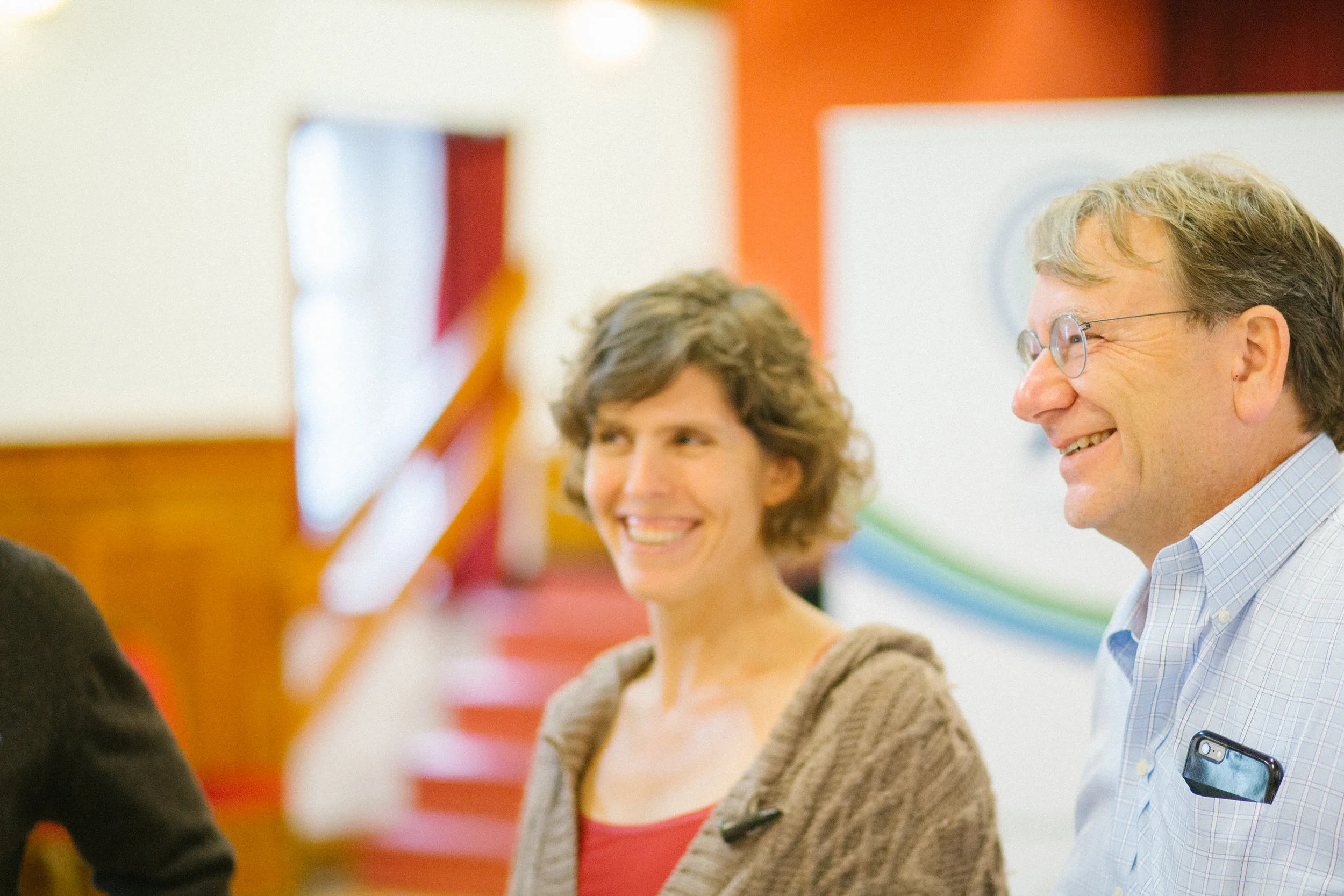 Two women and one man smiling and engaging in conversation at an indoor event, with colorful decorations in the background.