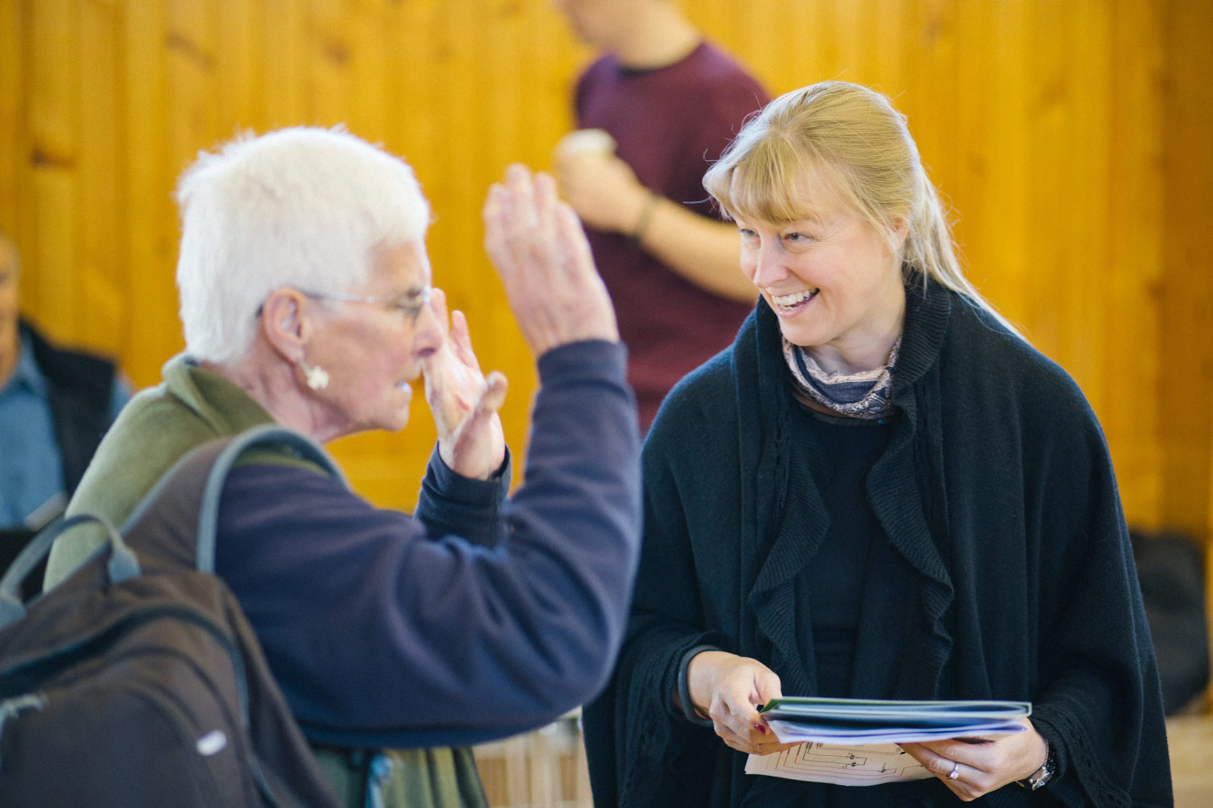 A woman smiling and high-fiving an elderly woman with white hair in a room with wooden walls.