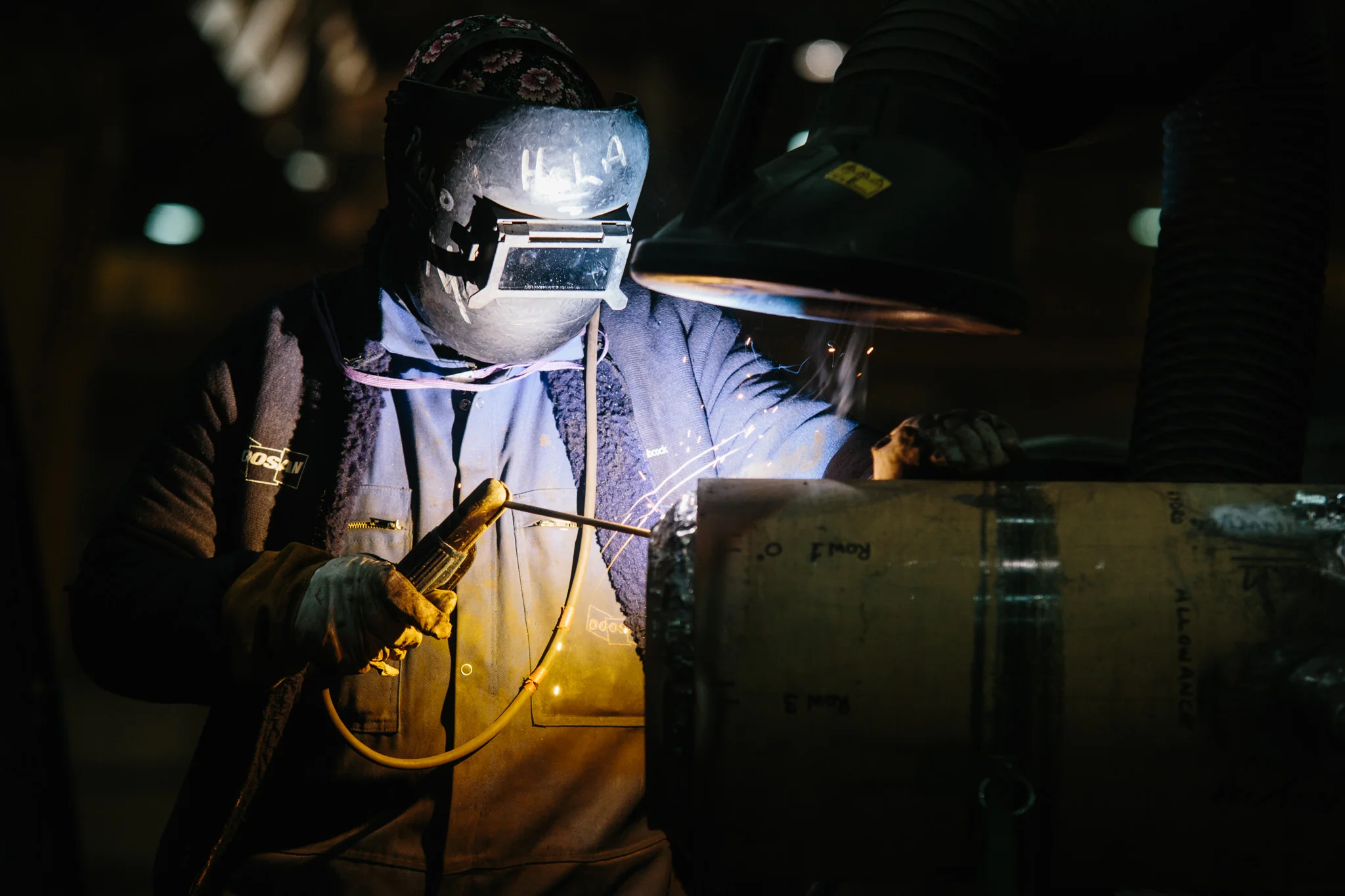A person welding metal in a dark workshop, wearing a welding helmet with a glow and protective gloves.