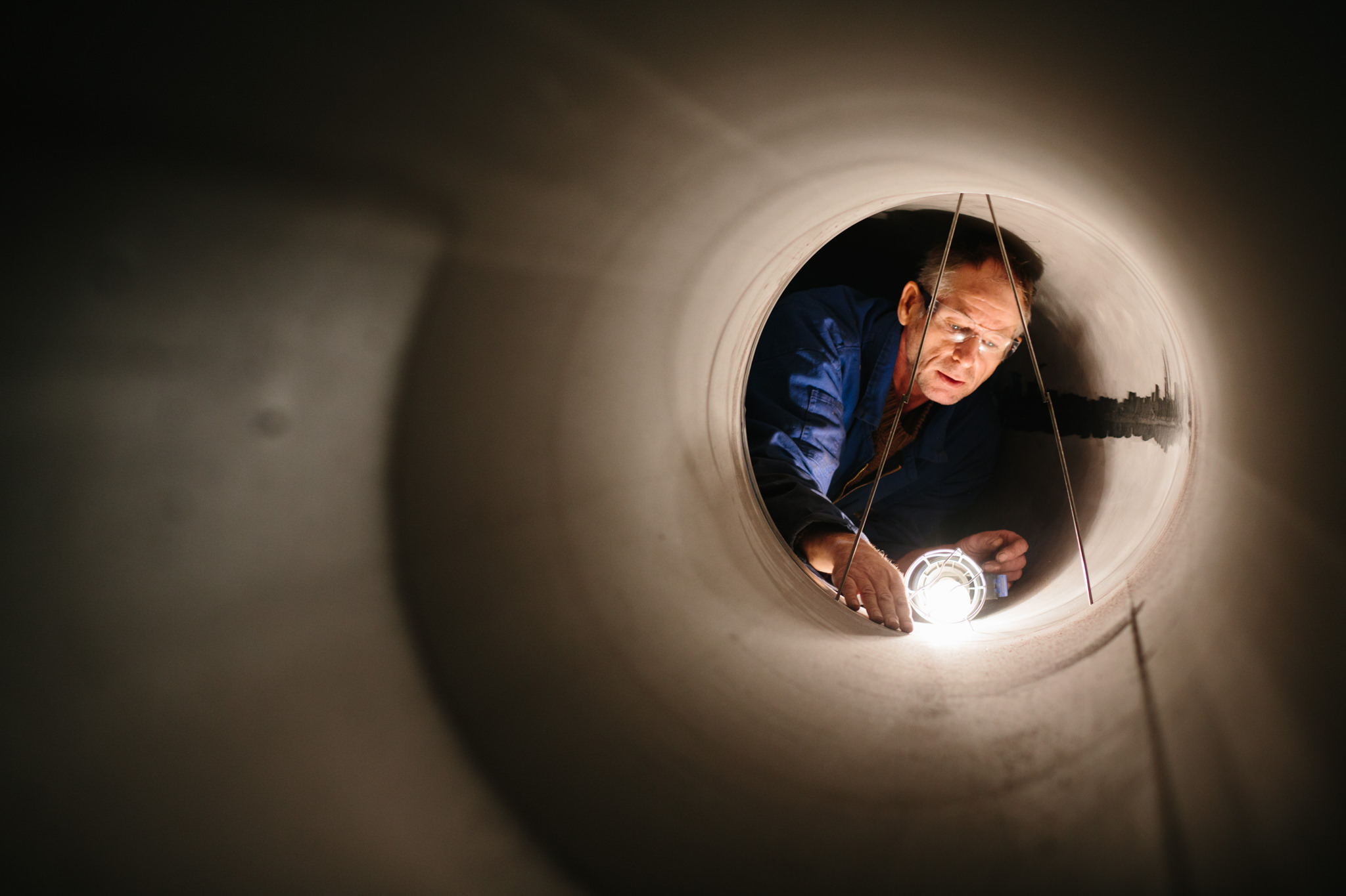 A man inspecting the interior of a large cylindrical pipe, with a light fixture creating illumination inside.