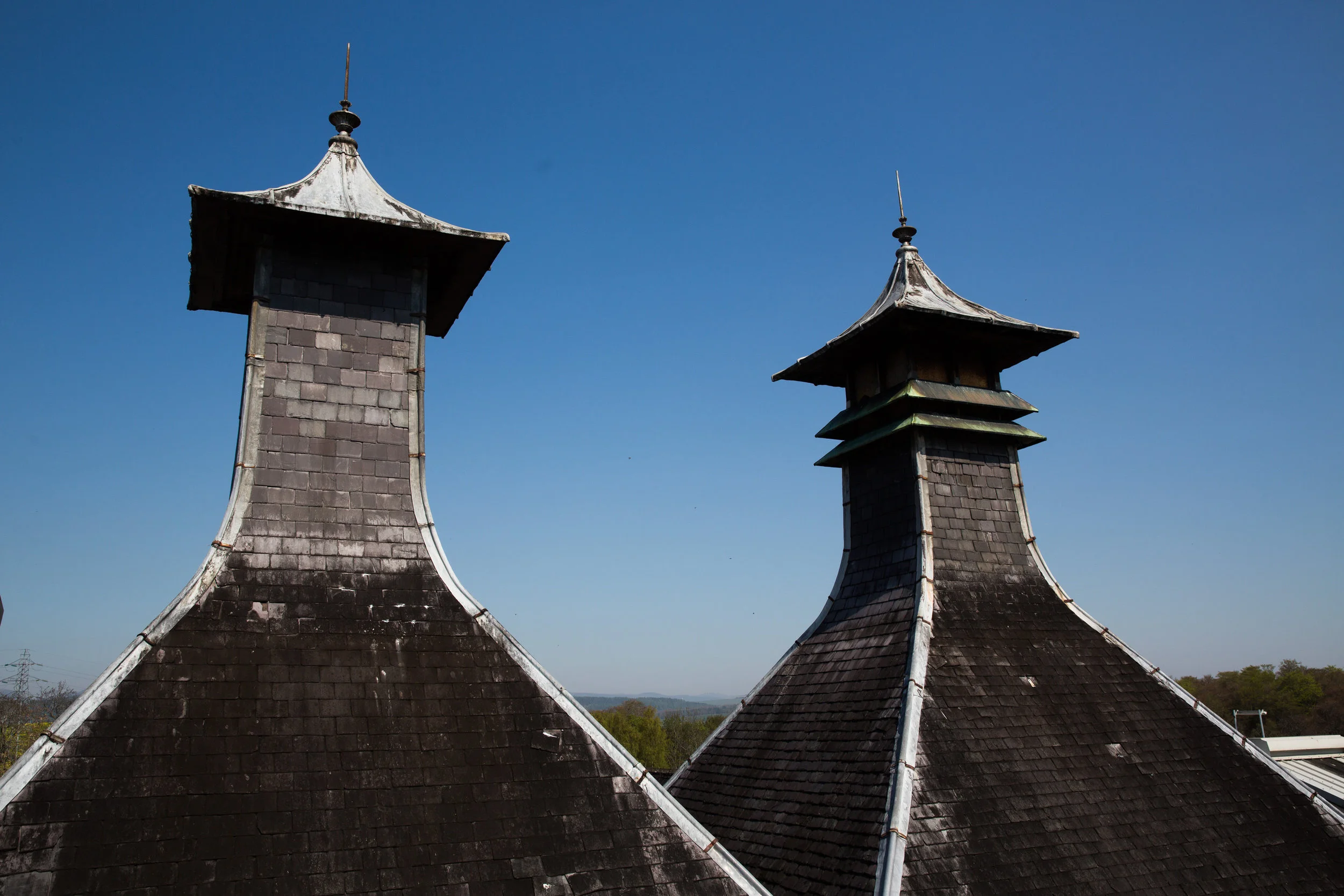 Two old rooftops with weathered shingles and ornate rooftop structures under a clear blue sky.