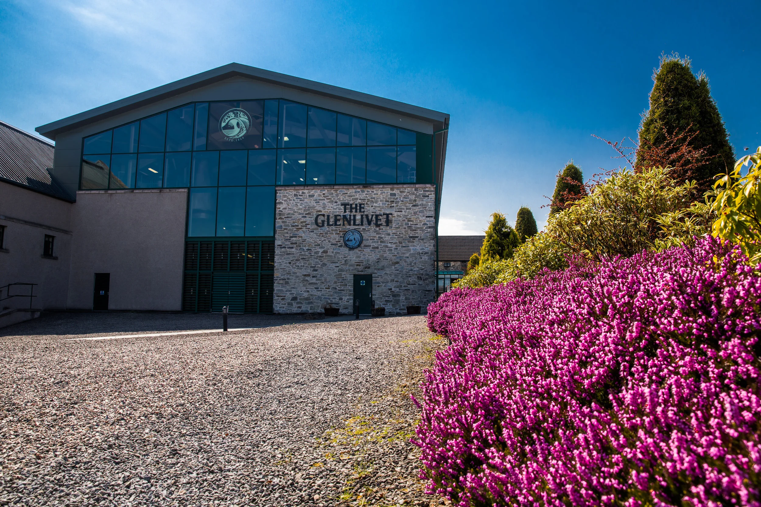 The Glenlivet building surrounded by pink flowering bushes under a clear blue sky.