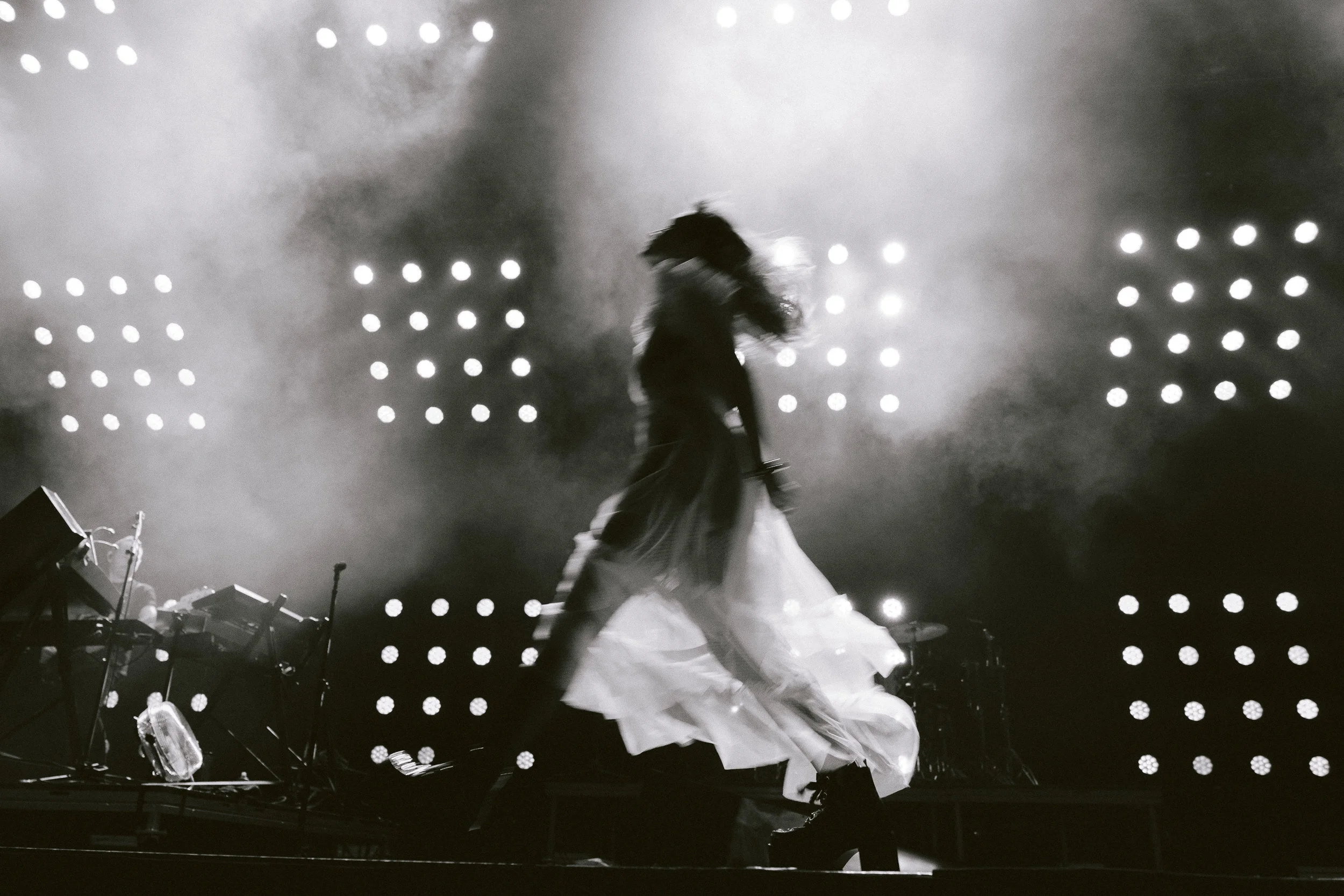 A silhouette of a performer on stage with bright stage lights behind them, creating a dramatic effect in black and white.