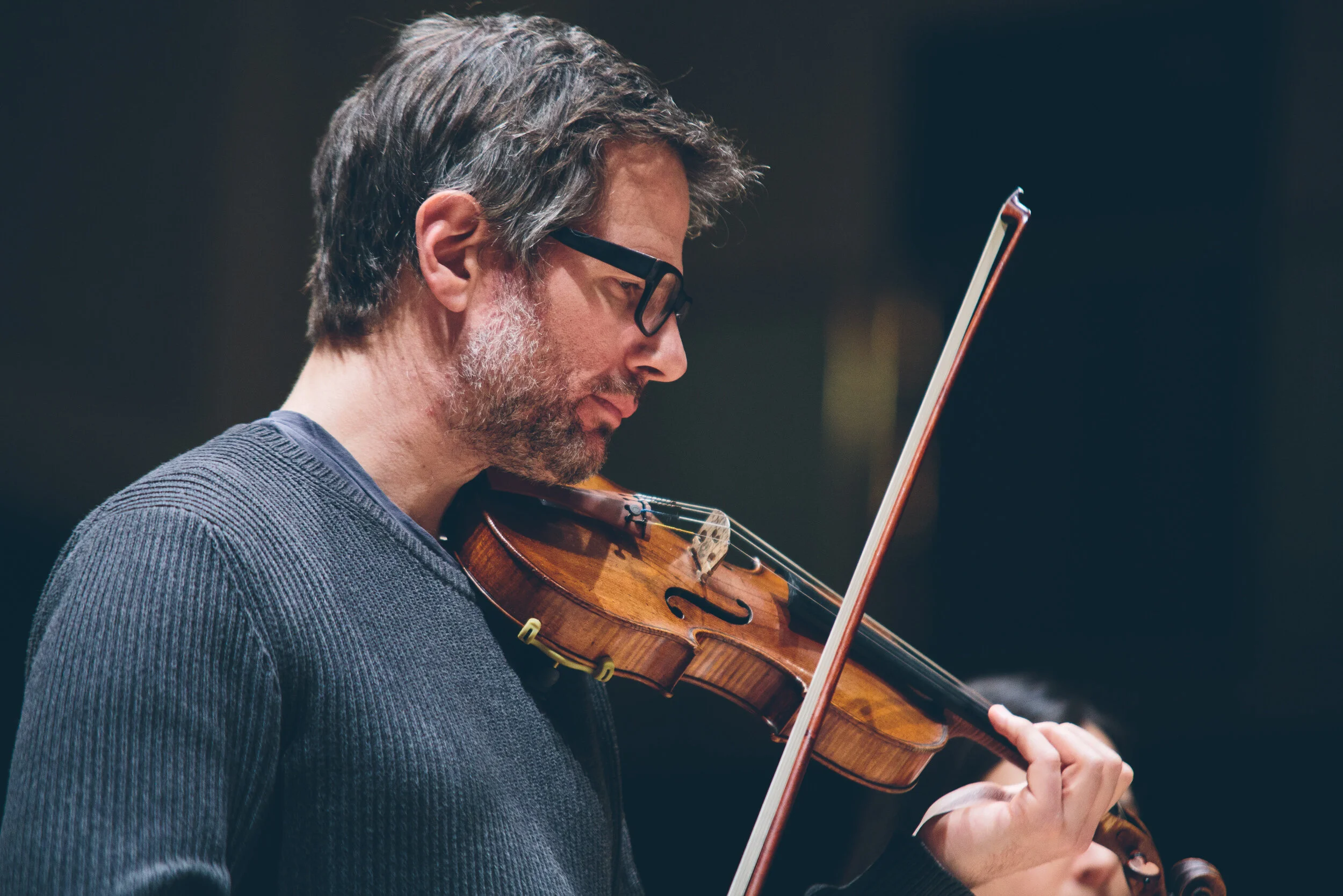 A man with glasses and gray hair playing a violin.