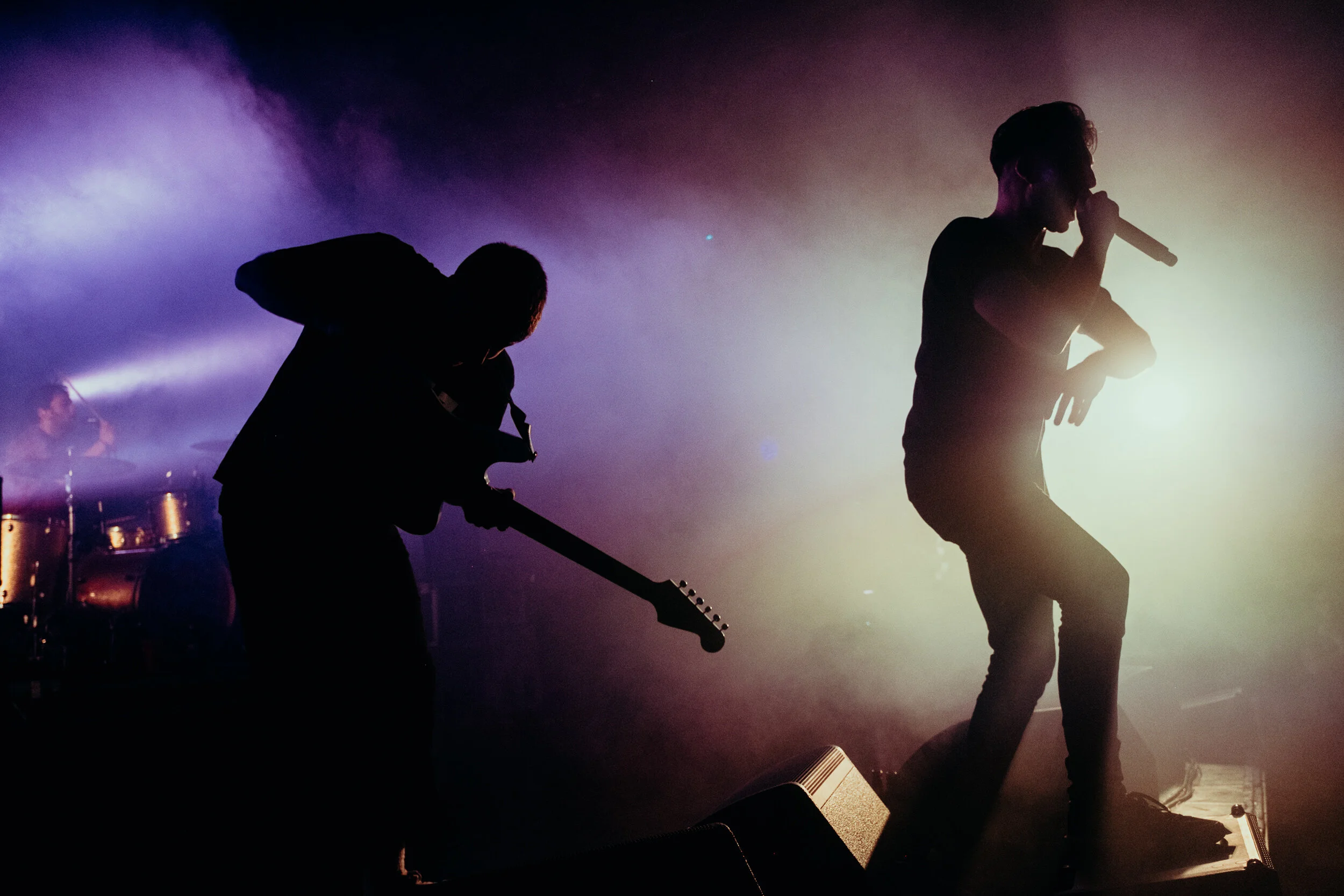 Silhouette of three musicians performing on stage with bright backlights creating a shadowed effect.