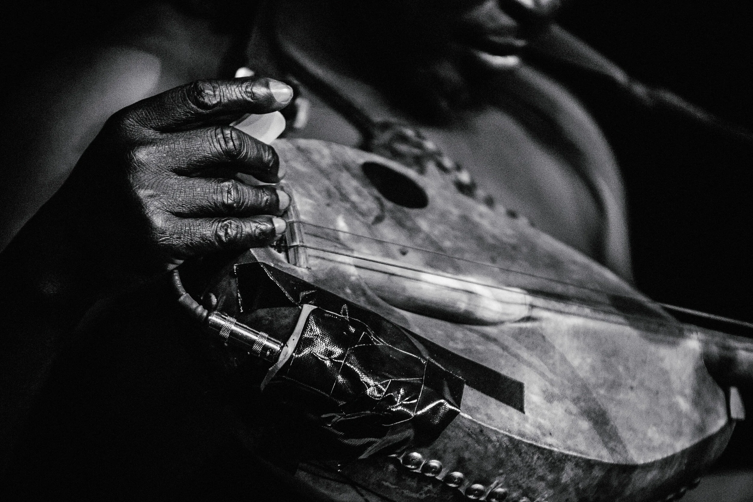 Close-up of a black hand holding a cassette tape, with part of the tape player visible, in monochrome.