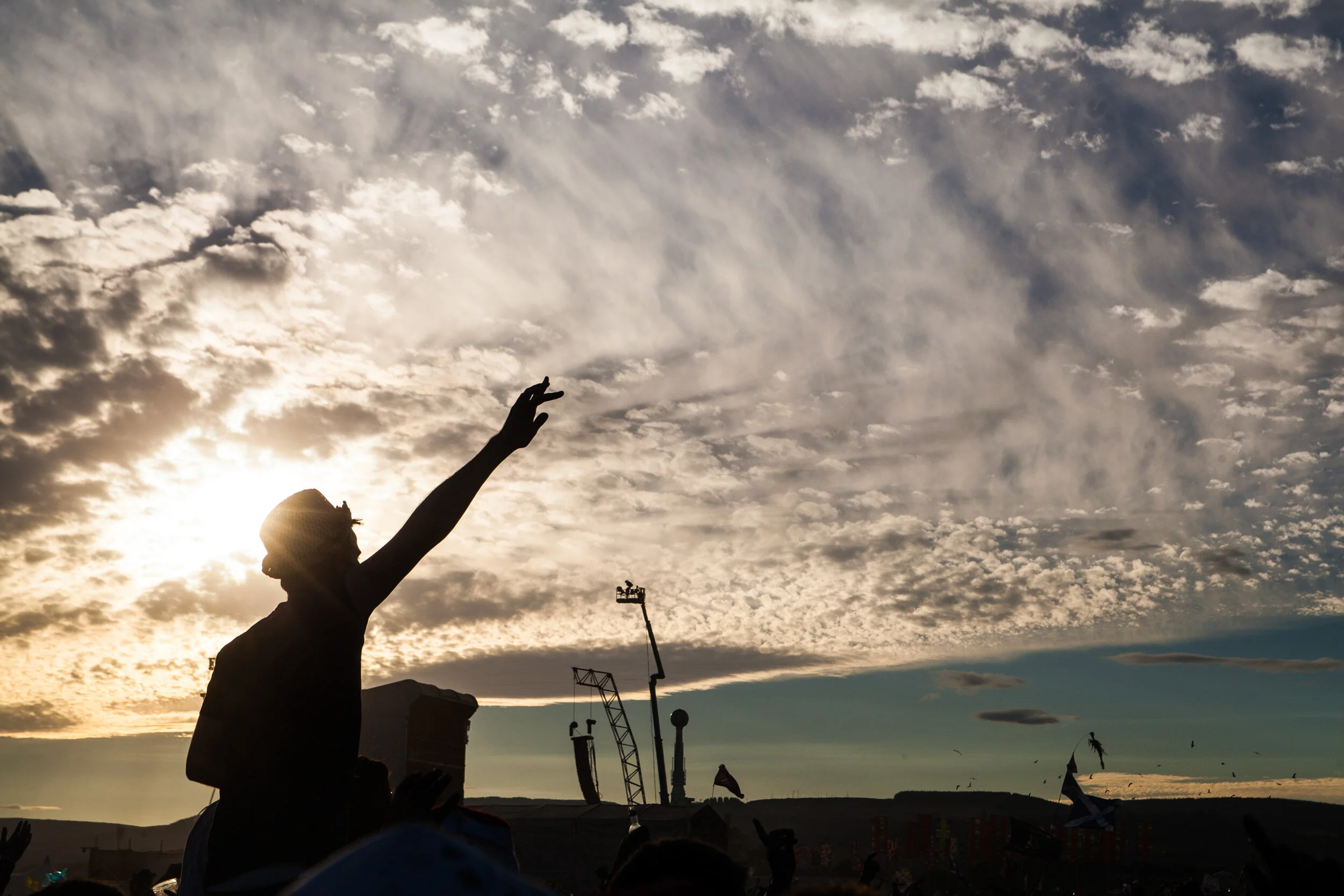 Silhouette of a person reaching towards the sky with clouds and the setting sun in the background.