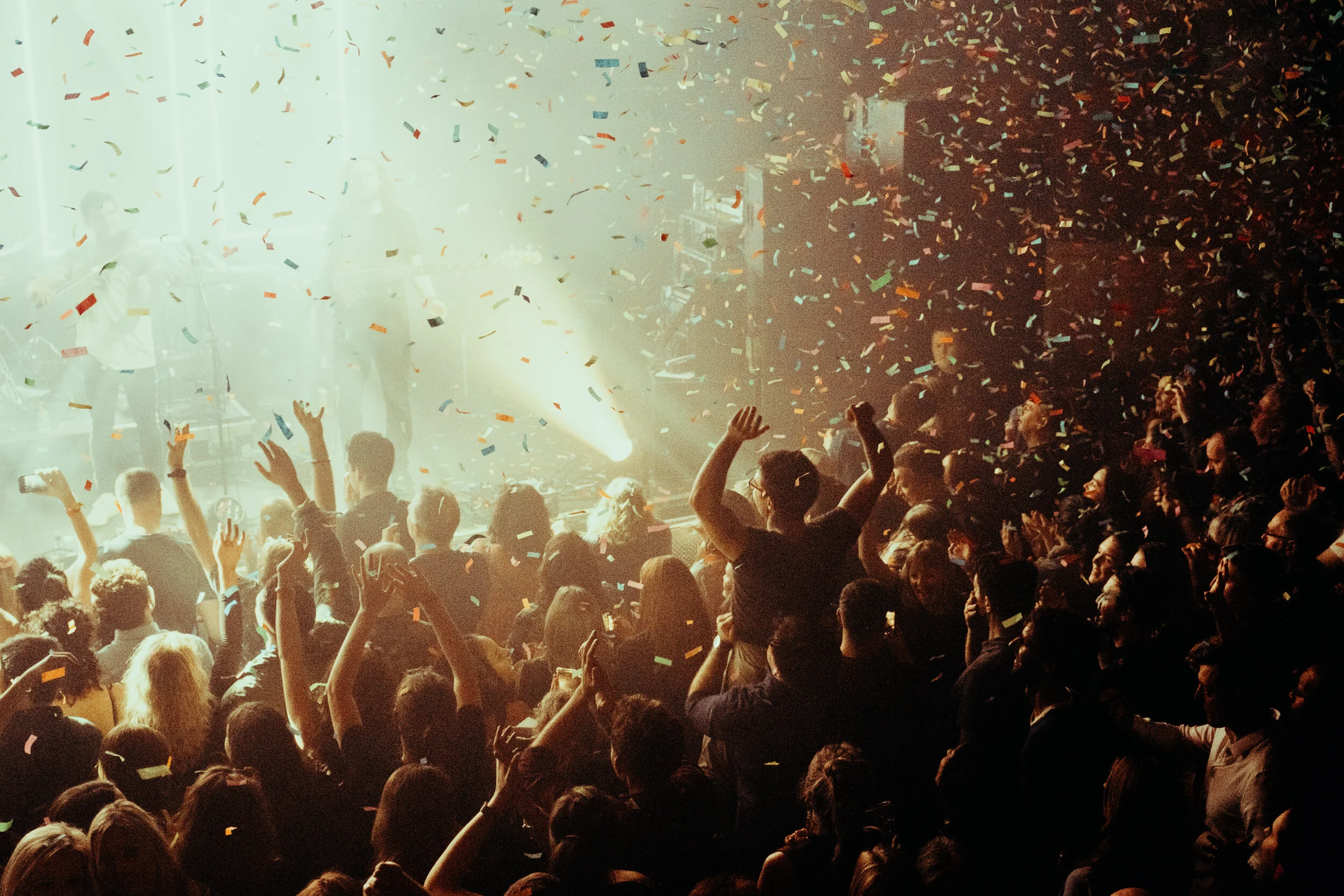 Crowd of people at a celebration or concert with confetti falling from above.