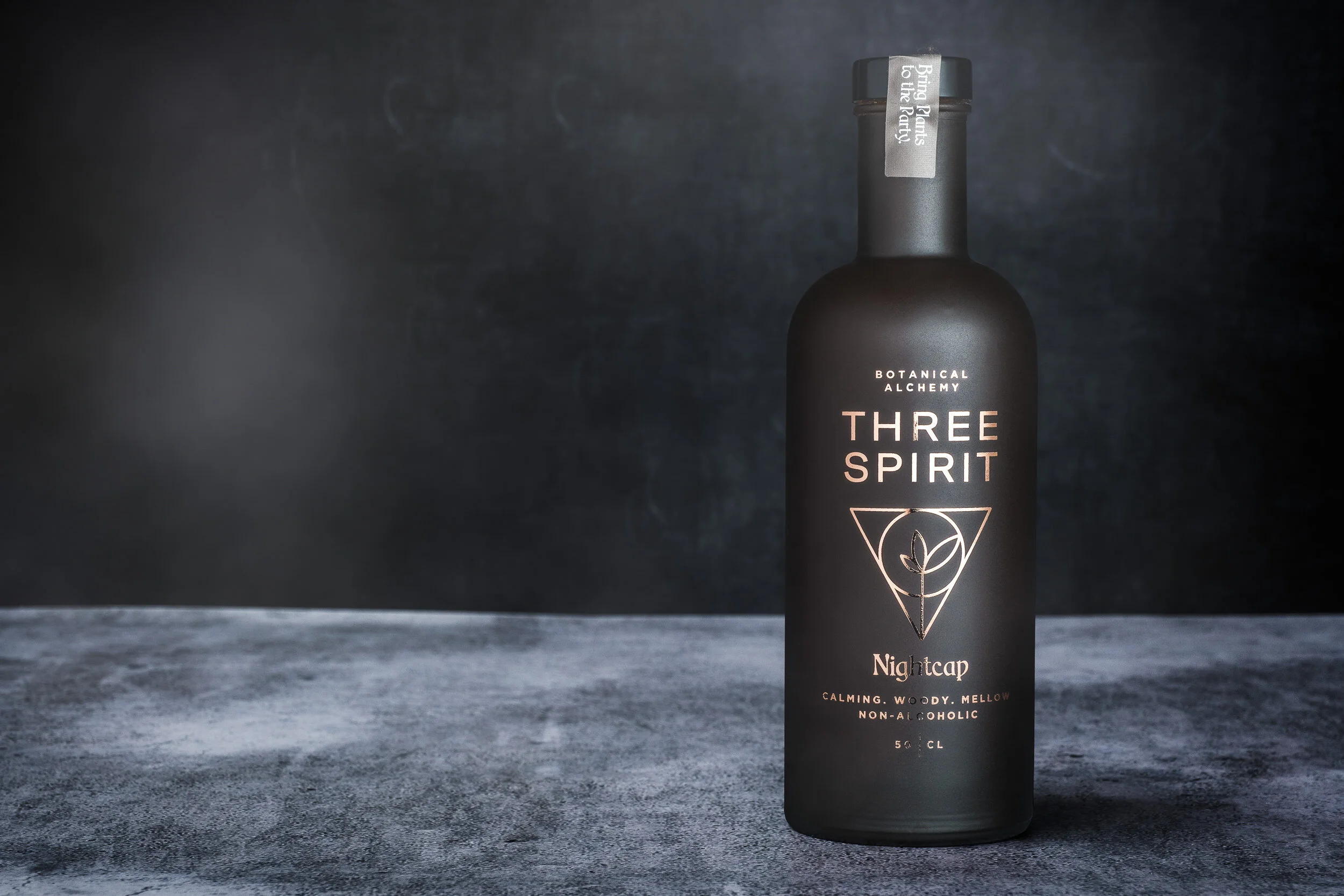 A black bottle labeled 'Three Spirit Nightcap' with a geometric design and plant illustration, set against a dark textured background.