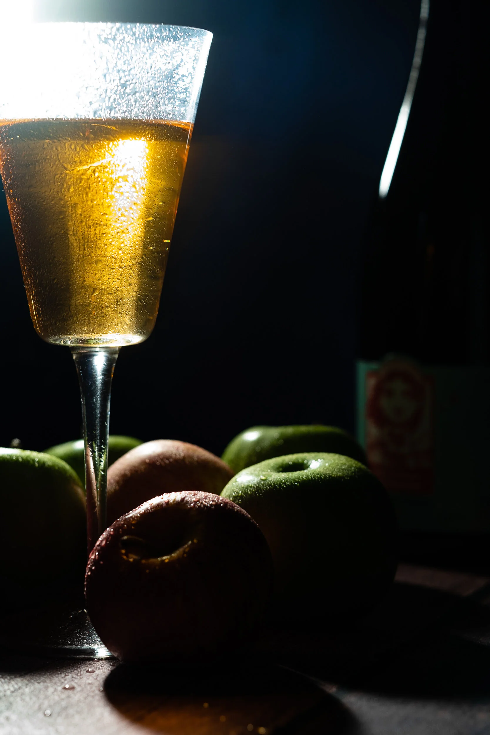 A glass of sparkling golden champagne with condensation on the outside, placed in front of a group of colorful eggs on a dark surface.