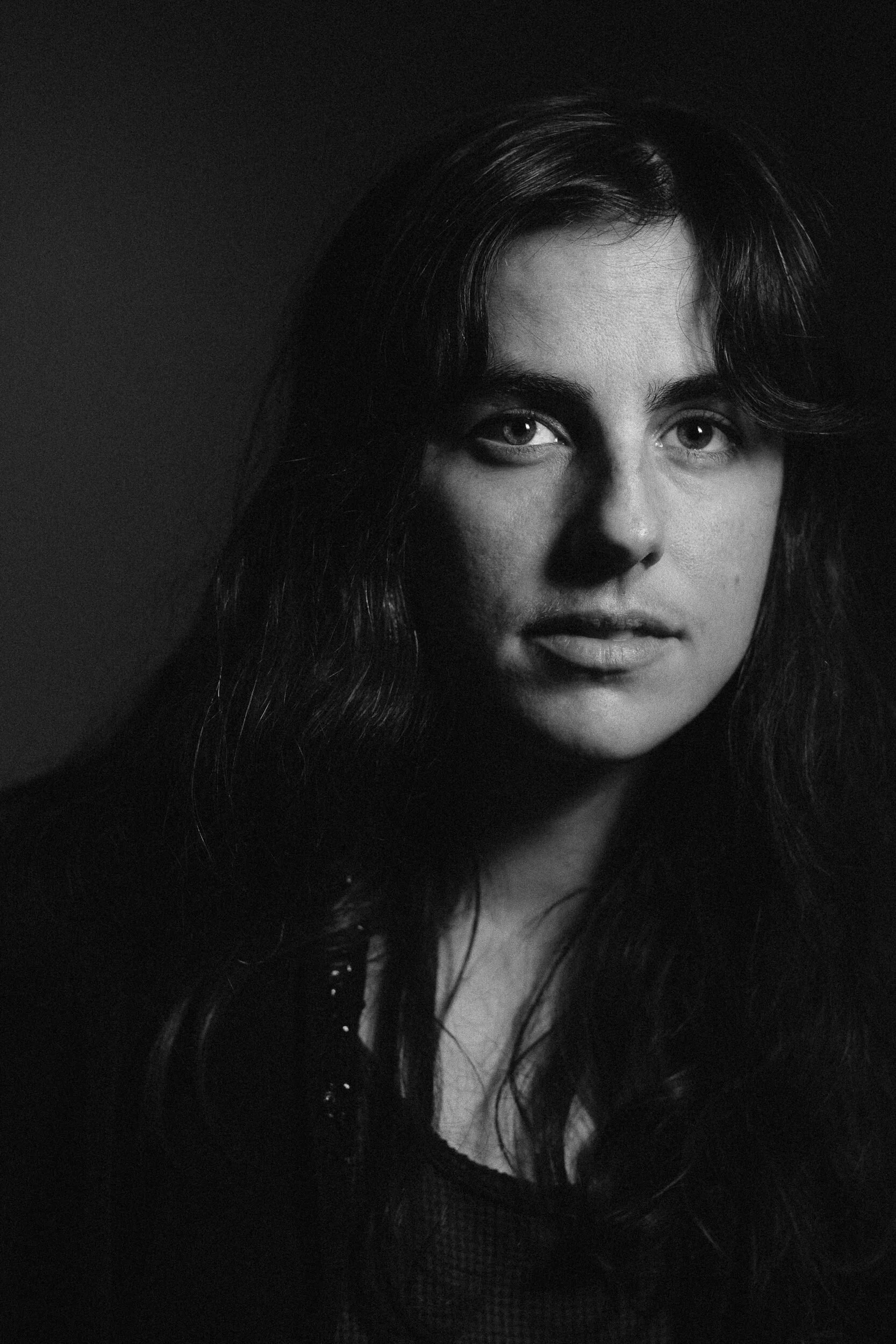 Black and white portrait of a woman with dark wavy hair, looking directly at the camera with a serious expression.