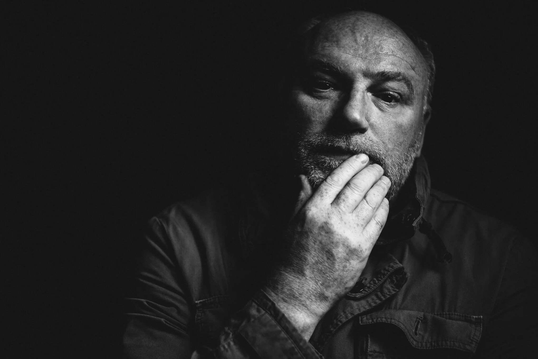 Black and white portrait of an older man with a beard and bald head, resting his chin on his hand in a thoughtful pose.