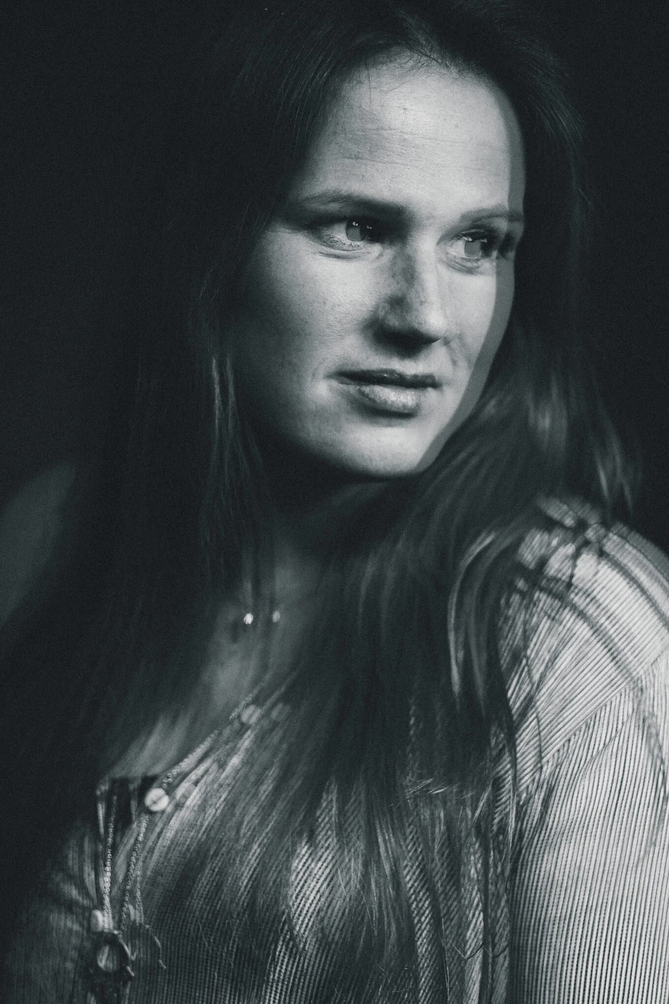 Black and white close-up portrait of a woman with long hair, looking to the side with a serious expression.