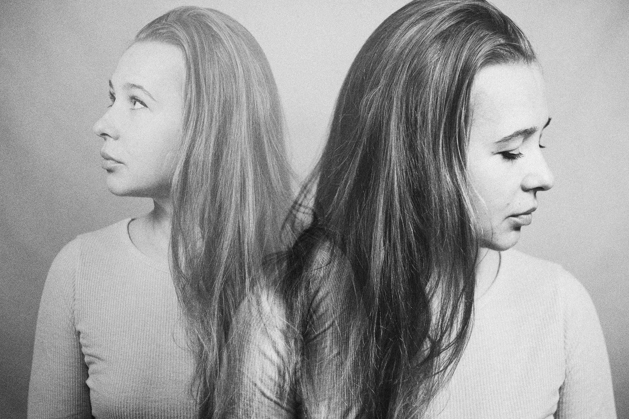 Black and white photo of two women with long hair, facing opposite directions with eyes closed.