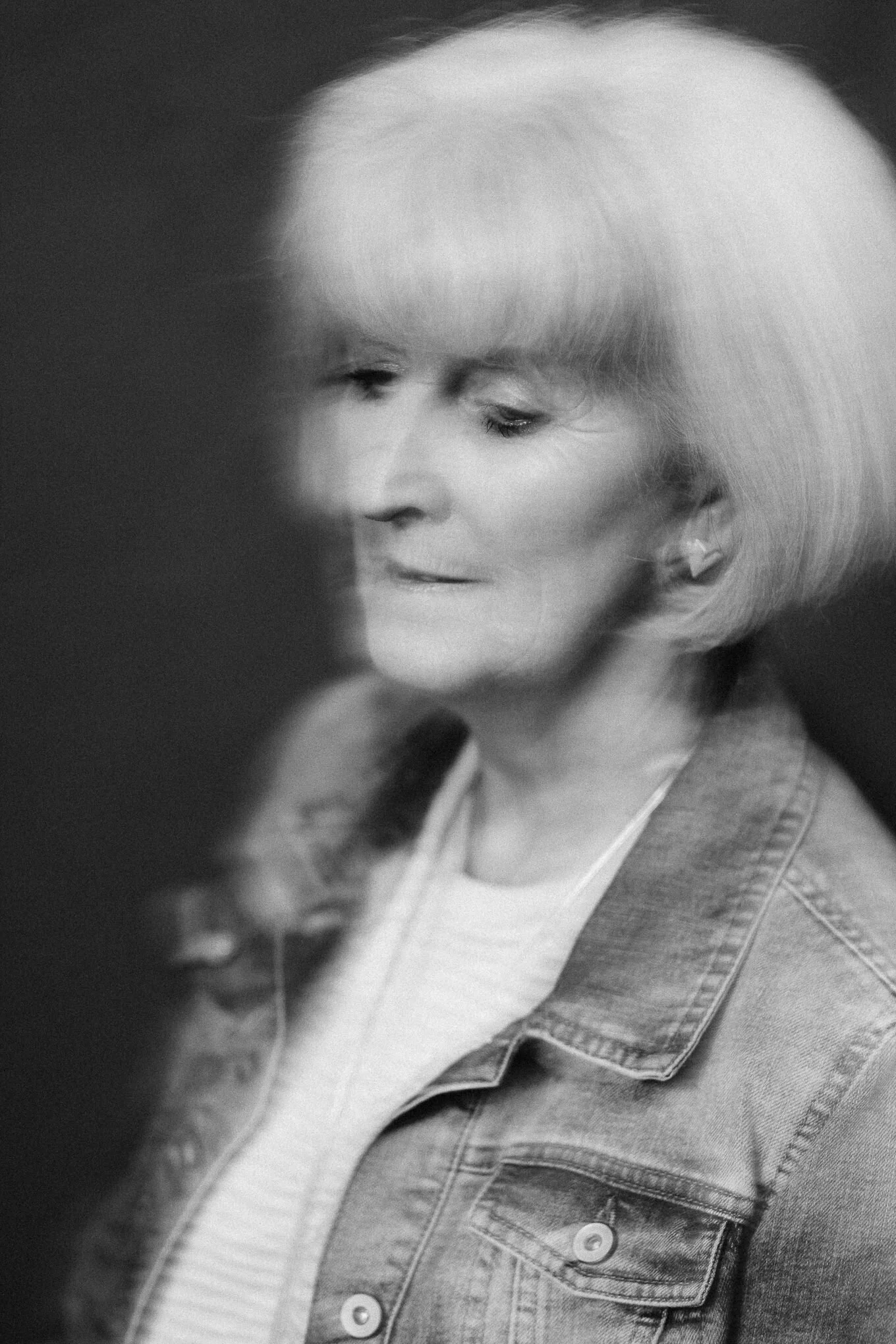 Close-up of a young girl with light-colored hair, wearing a denim jacket and a striped shirt, looking down thoughtfully.