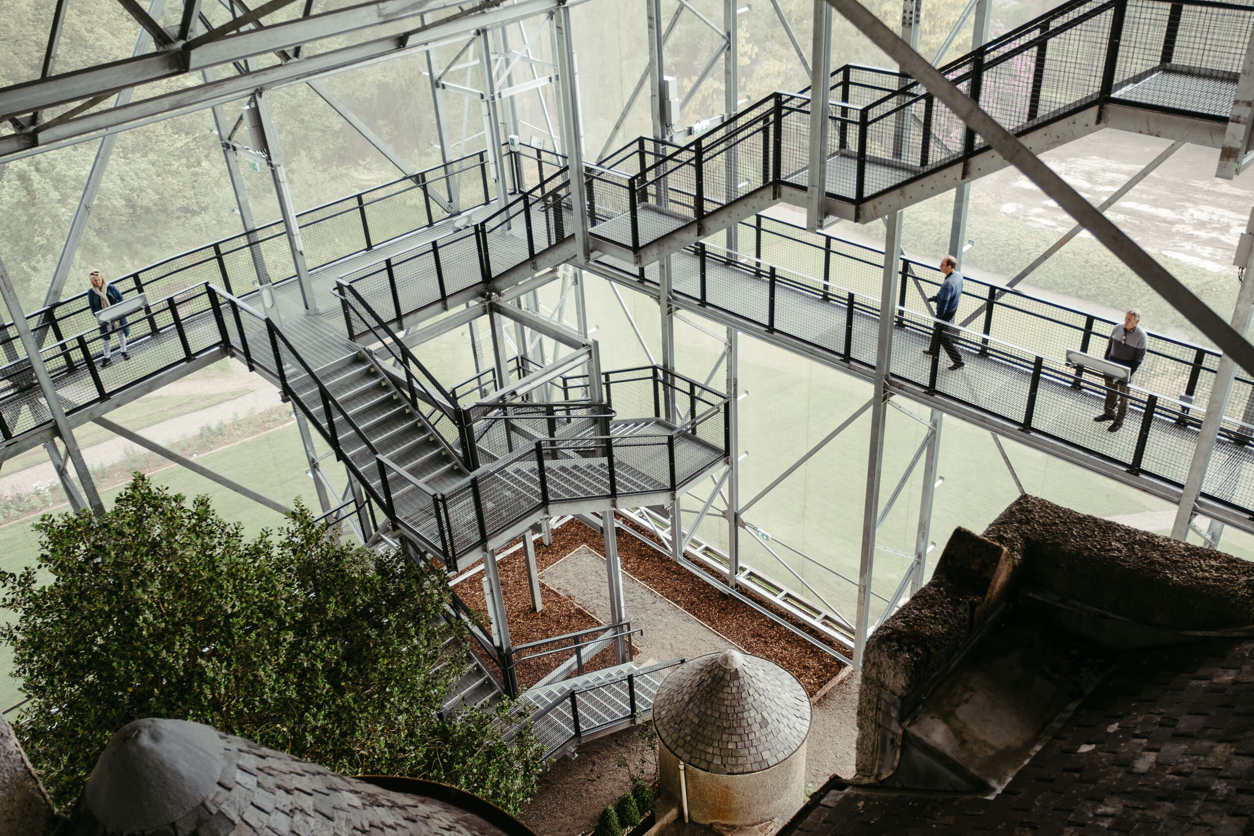 A view of a metal fire escape staircase with black railings outside a building, with several people walking on it, overlooking a green landscape.