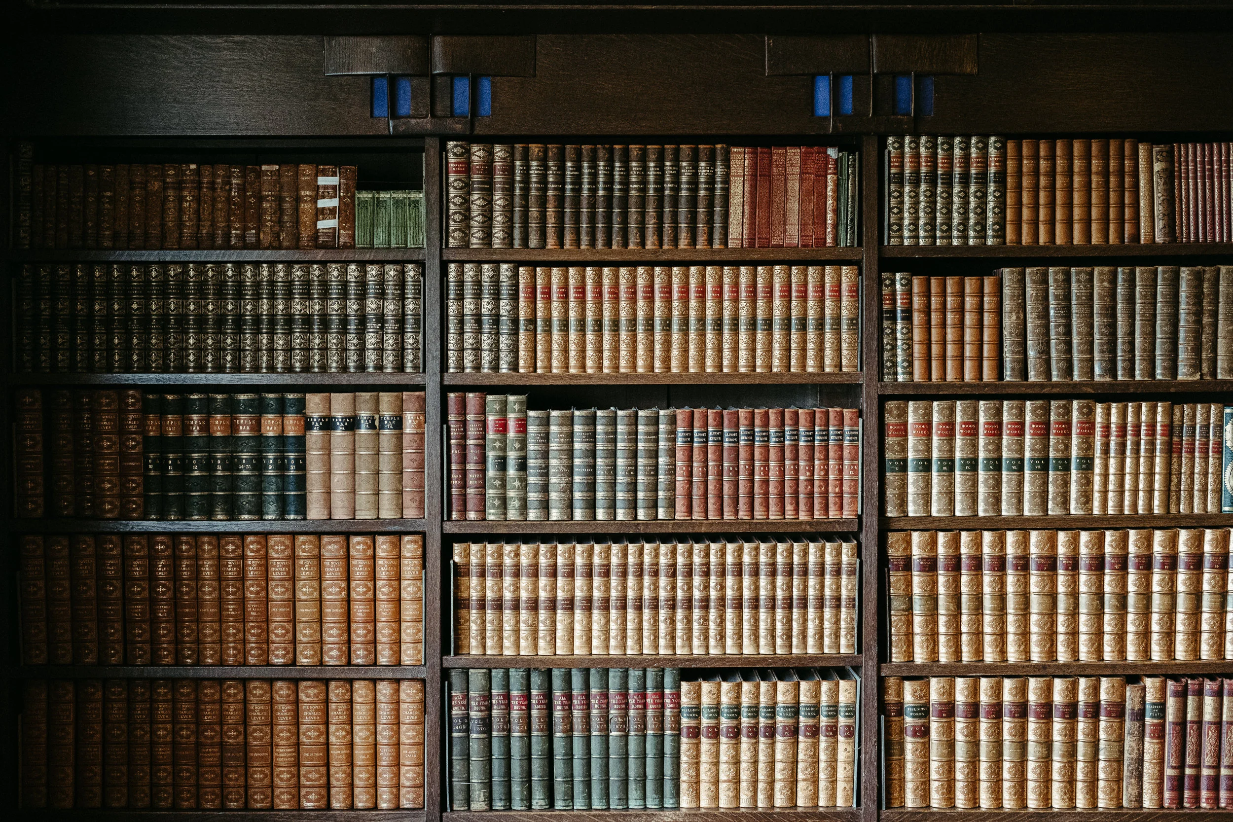 A wooden bookshelf filled with numerous hardcover books, arranged in neat rows with diverse sizes and colors.