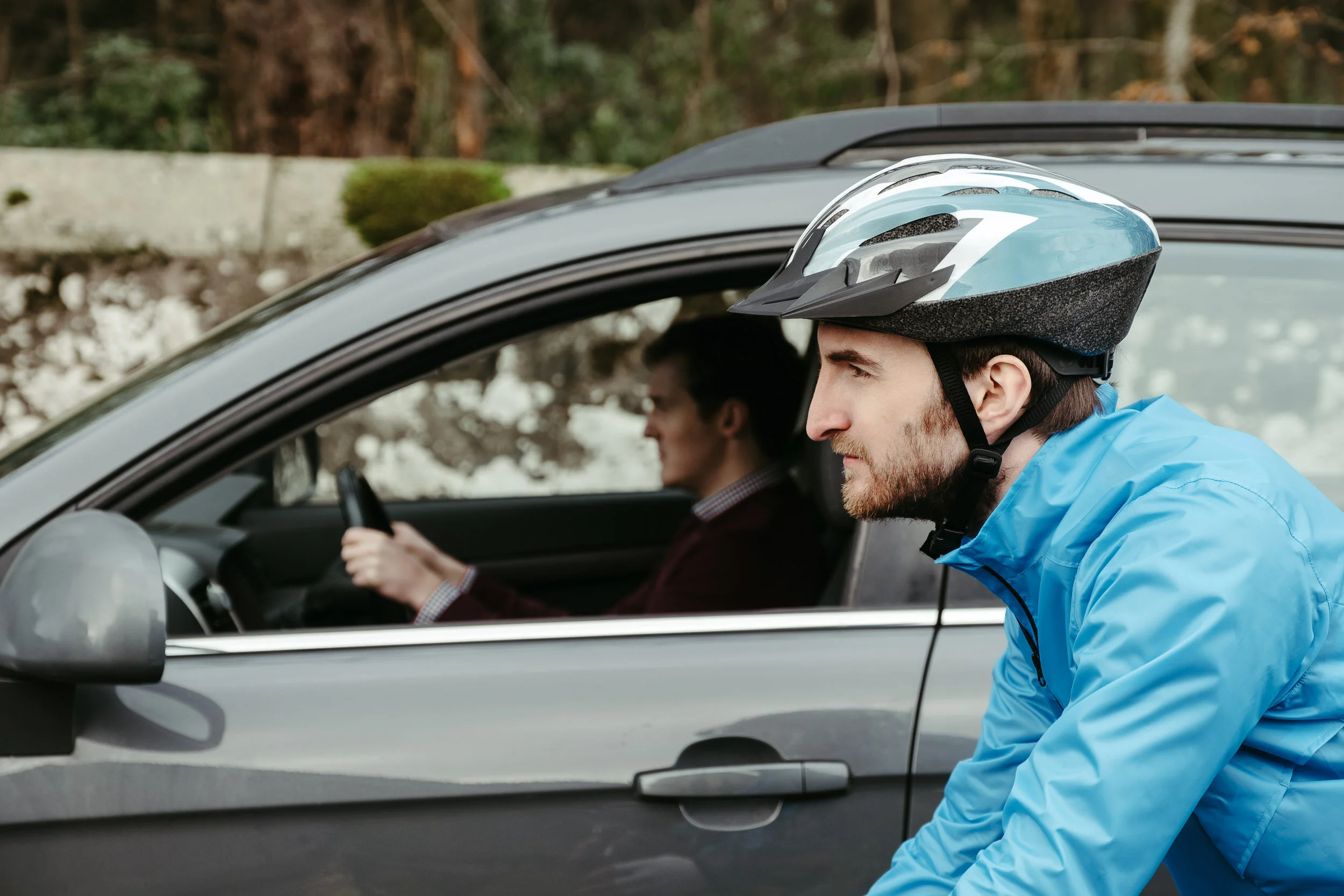 A man in a blue jacket and bicycle helmet leaning into a car while a woman in the driver’s seat focuses on the steering wheel.
