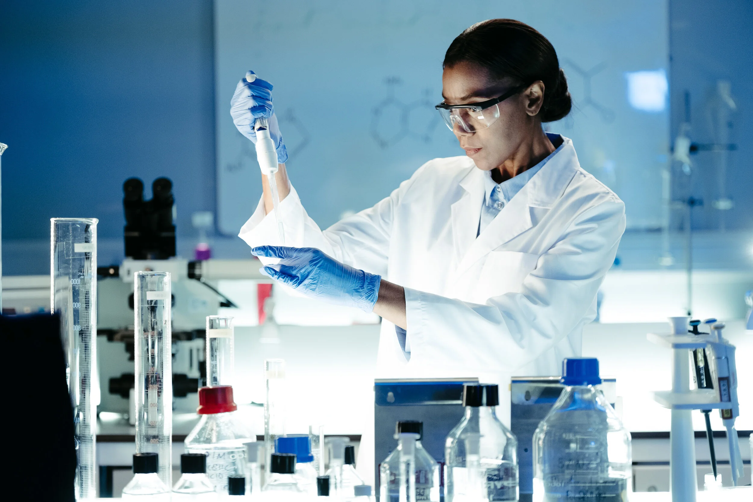 Scientist in safety goggles and gloves working with test tubes and laboratory equipment in a scientific lab.
