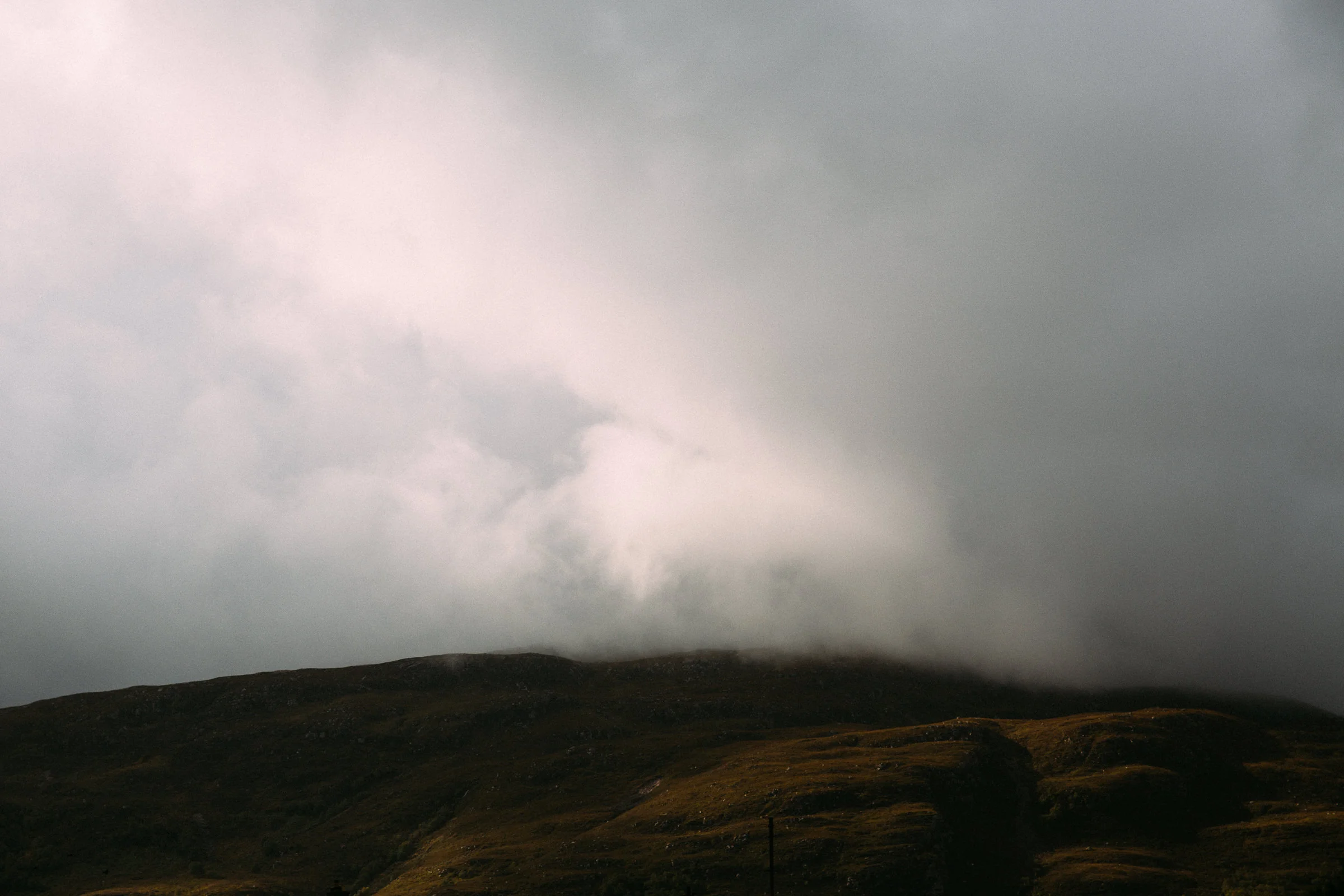 Dark cloudy sky over rolling hills with sparse vegetation, possibly during late afternoon or evening.