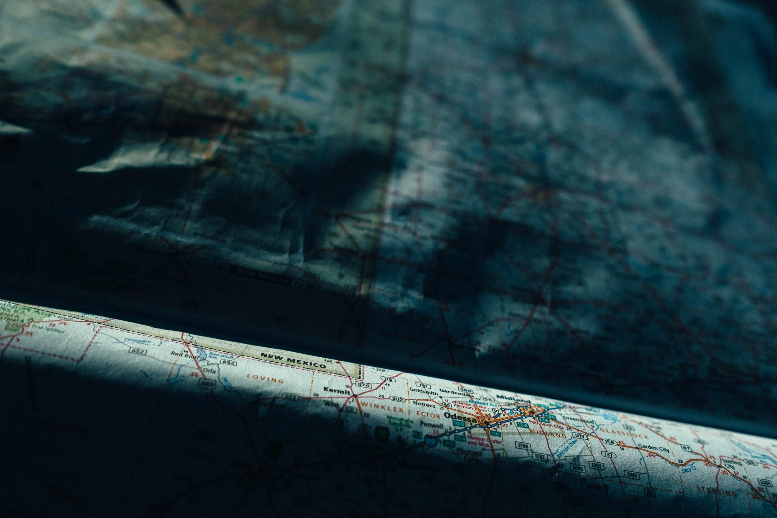 A partially visible paper map showing regions of Oklahoma, Texas, and New Mexico, with a dark, semi-transparent overlay covering part of it.