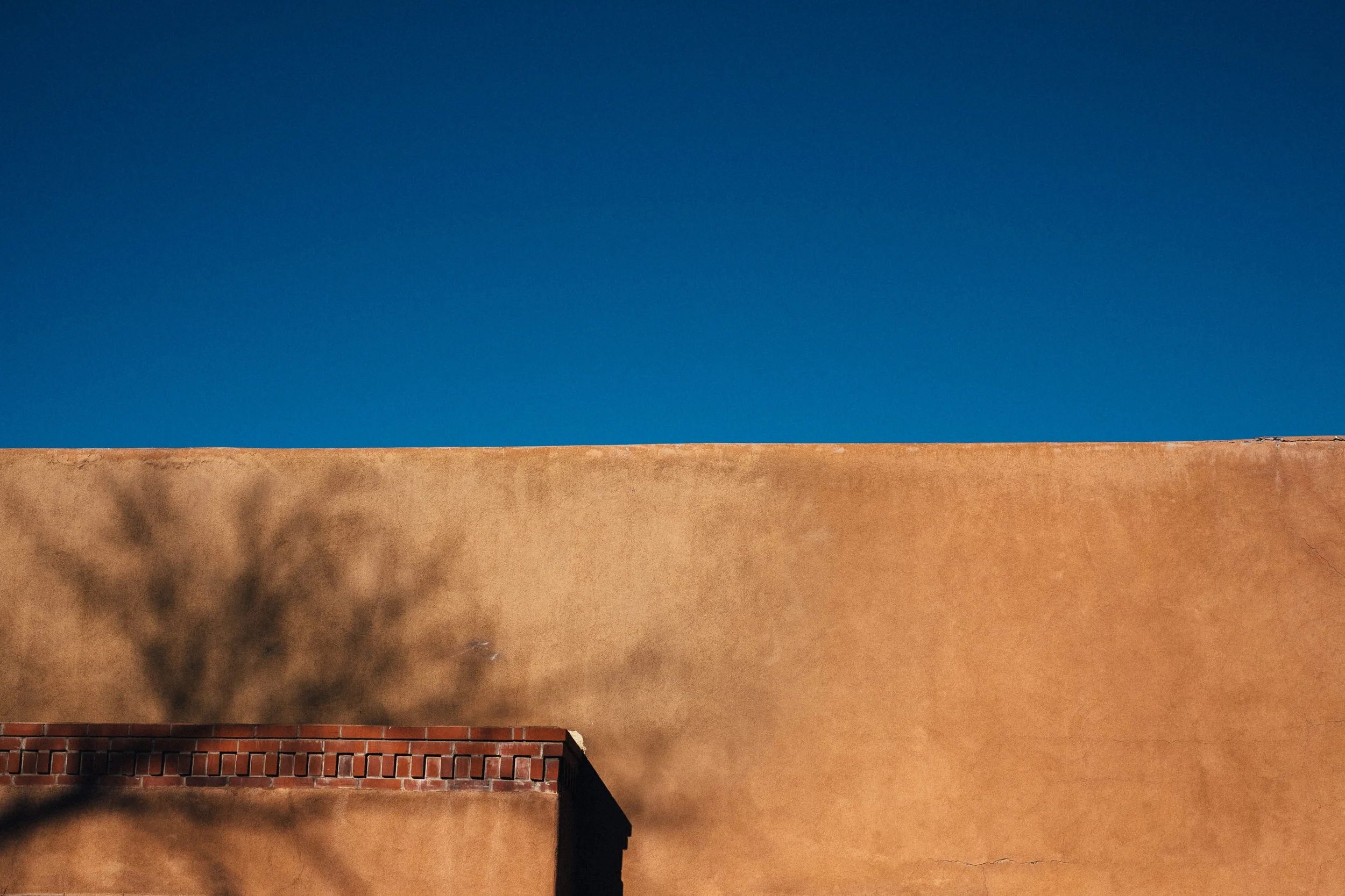A wall with a red brick section at the bottom and a tan stucco section on top, with the clear blue sky above.