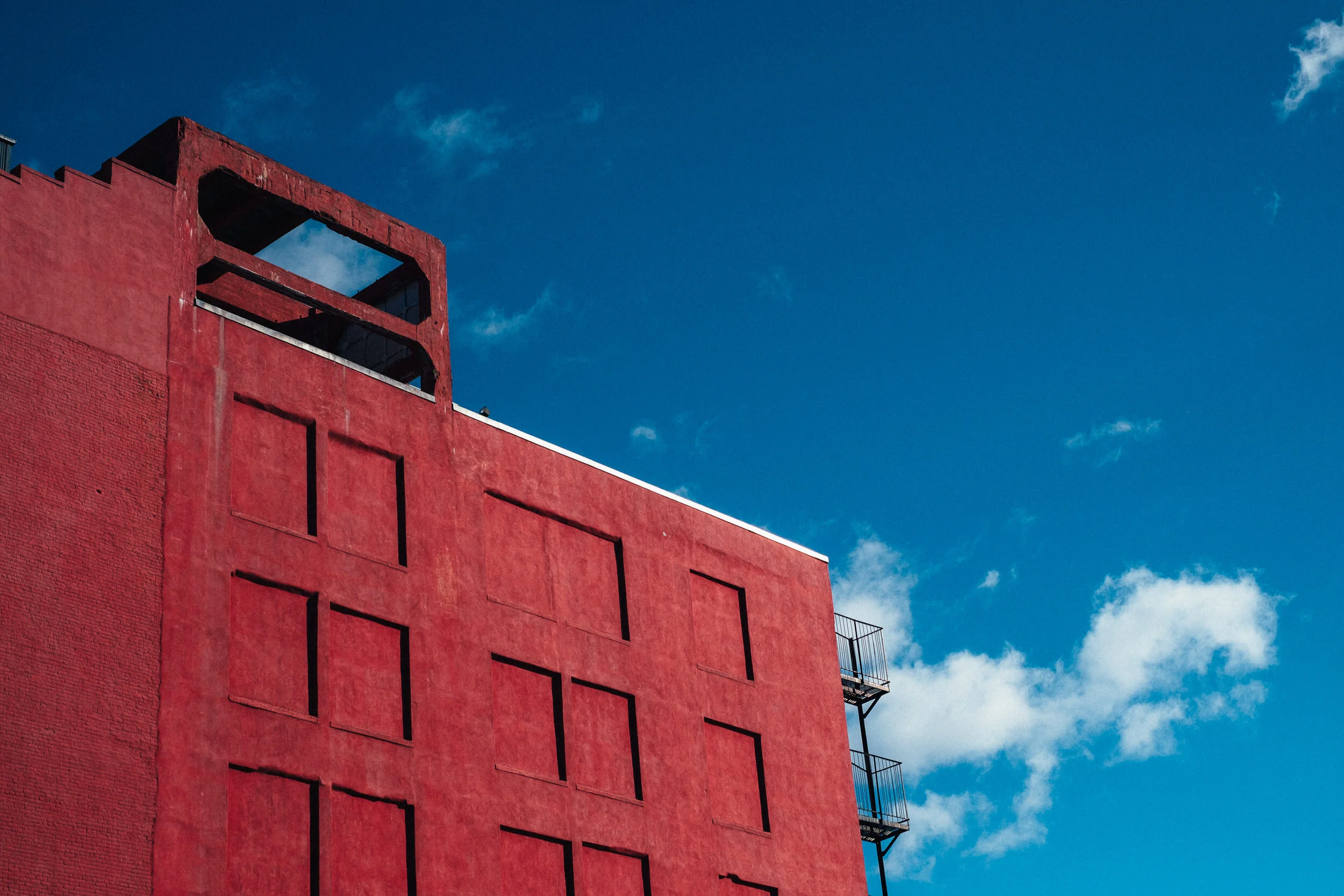 A red building with a rectangular cutout near its top, set against a blue sky with some clouds.