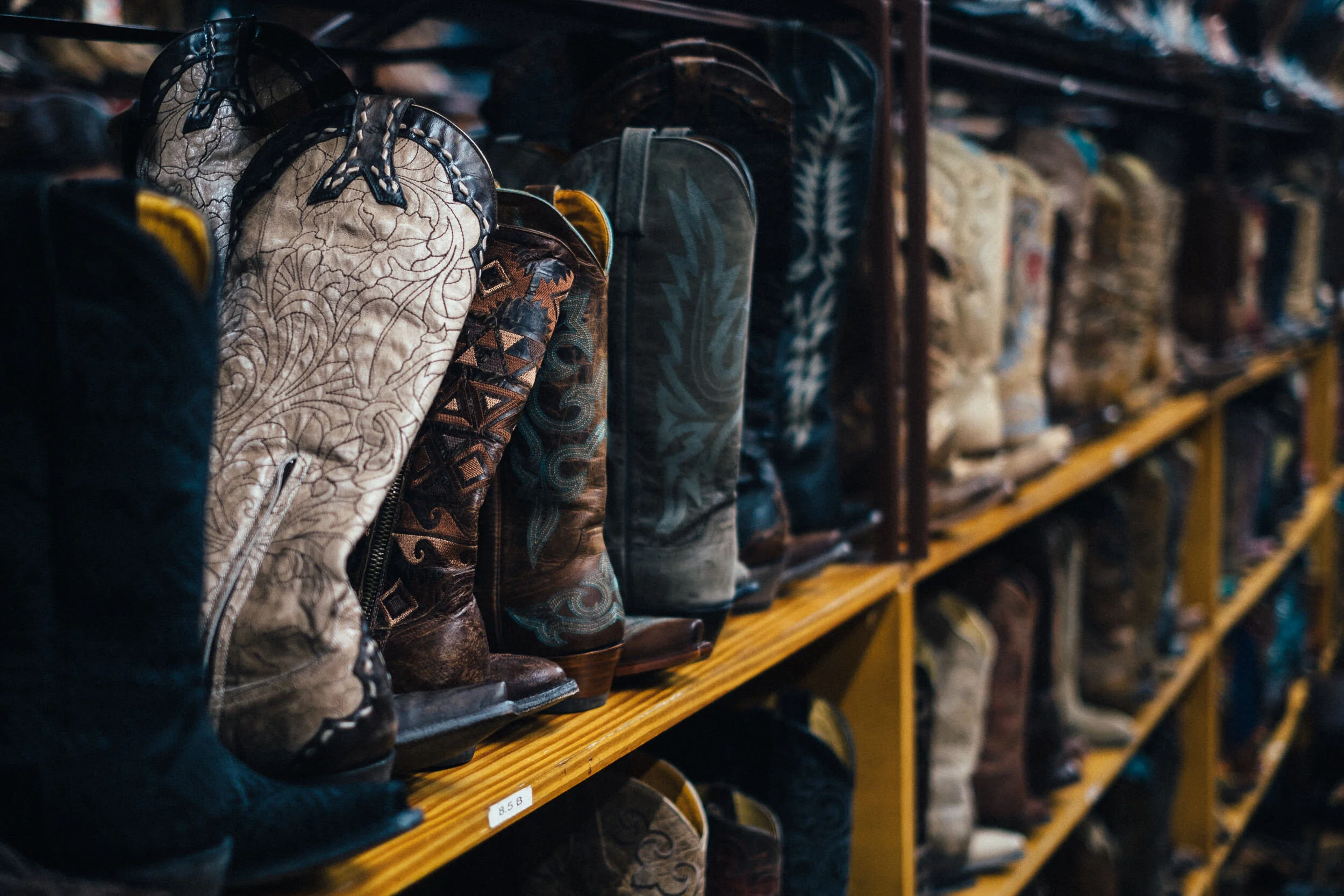 A store shelf displays cowboy boots with various colors and patterns, arranged in rows.