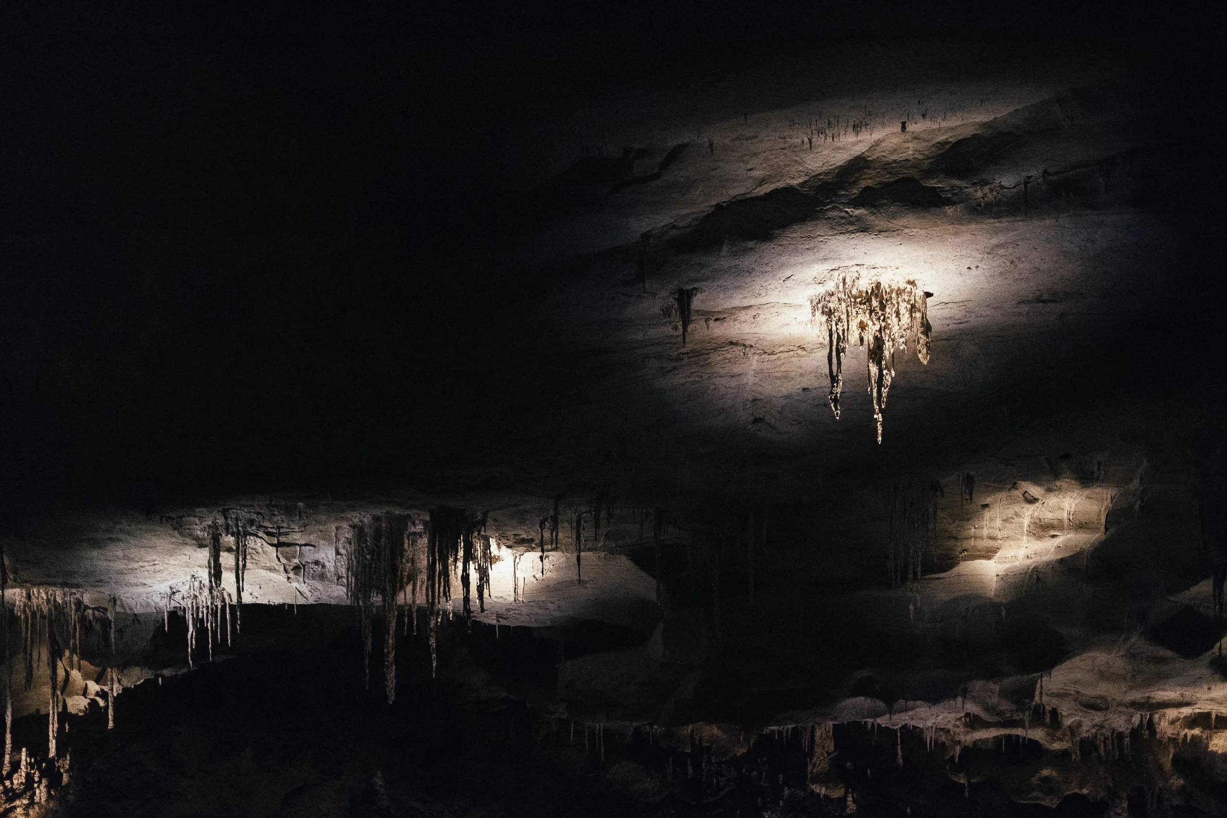 Views inside a dark underground cave with stalactites hanging from the ceiling, illuminated by subtle light.
